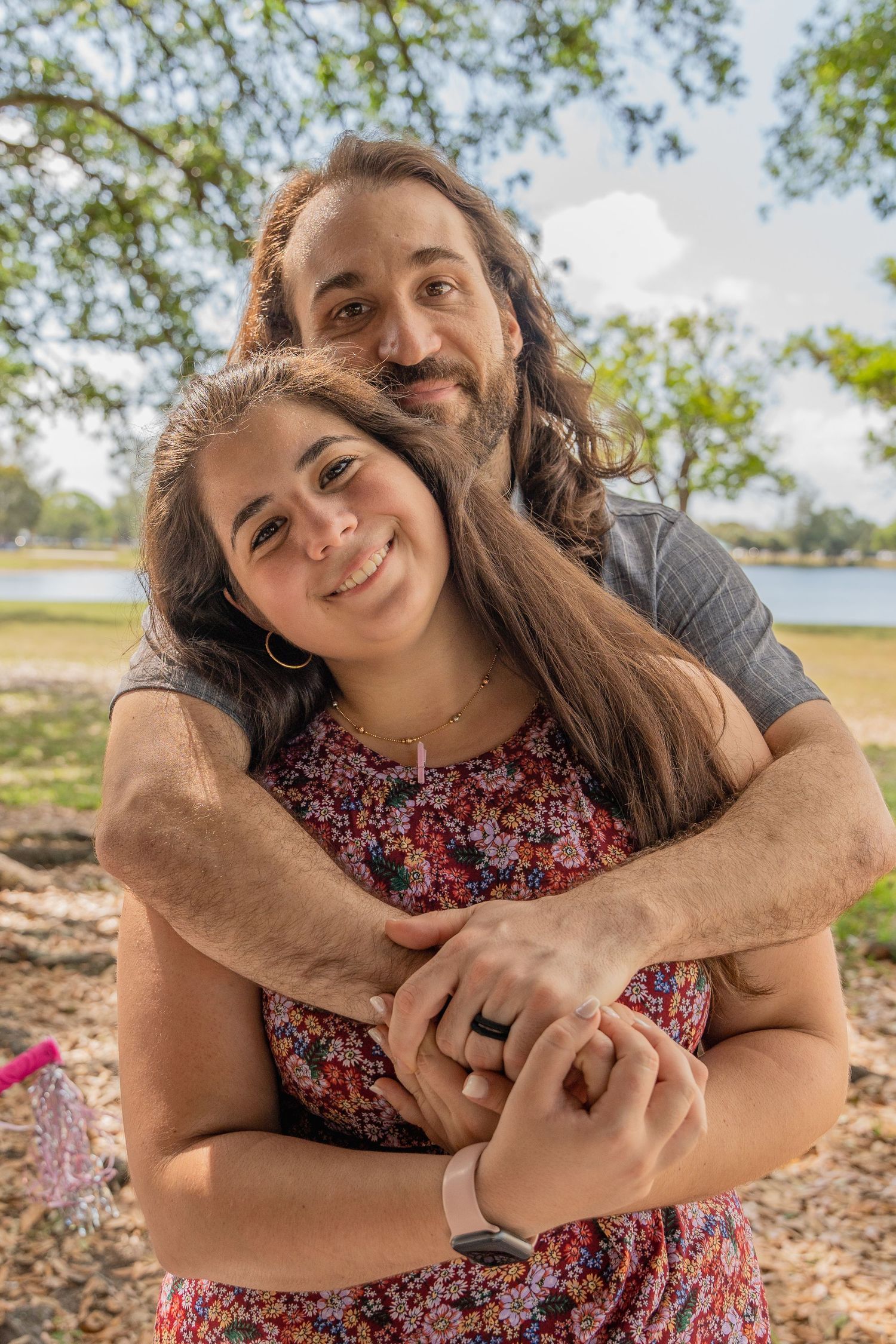 Couple embracing outdoors beneath trees during a casual South Florida maternity photo session.