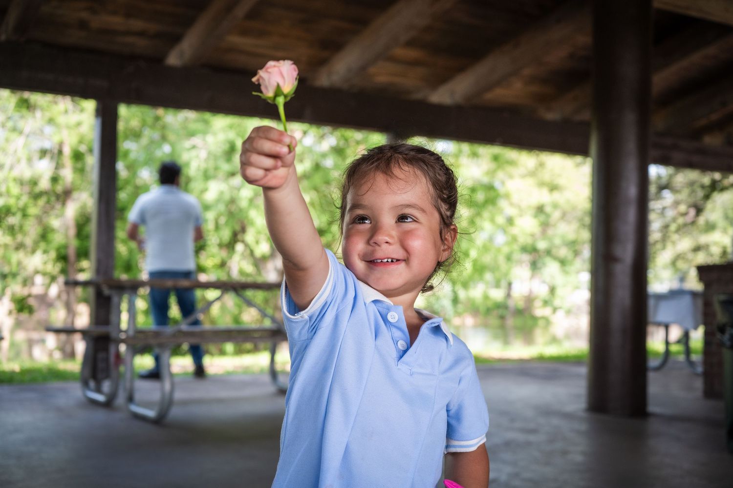 Smiling child holding a small flower during an outdoor baby shower celebration under a pavilion in South Florida.