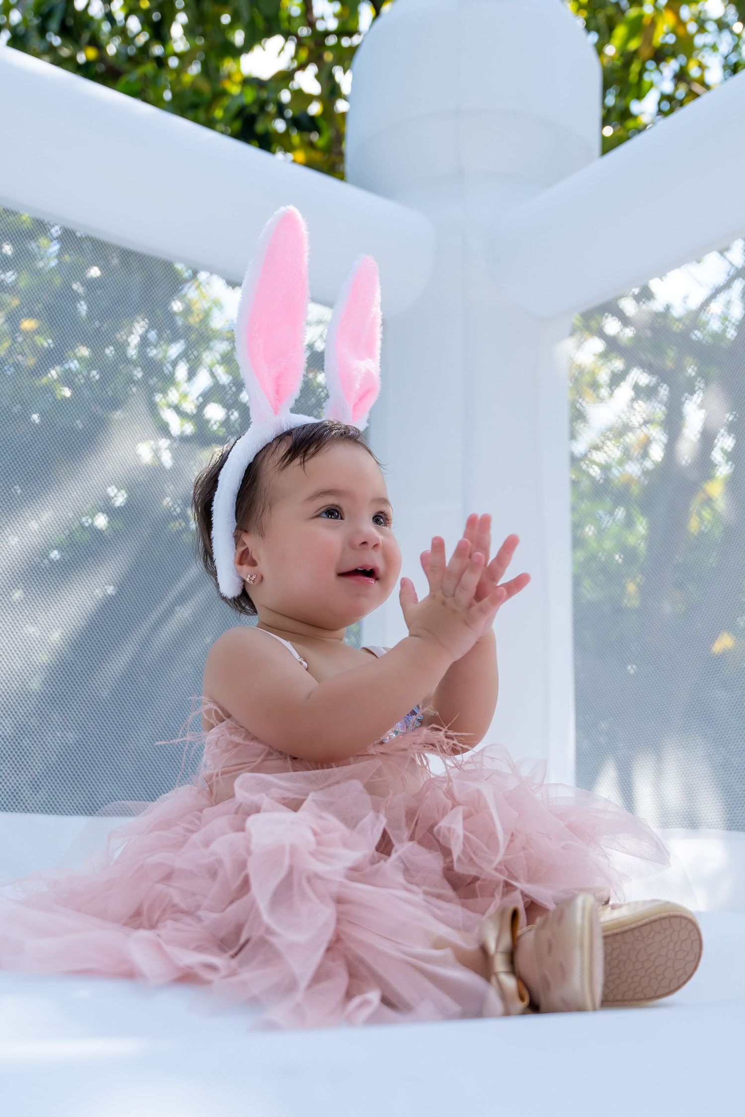 First birthday portrait of a baby girl wearing bunny ears and a pink dress during a whimsical birthday setup.