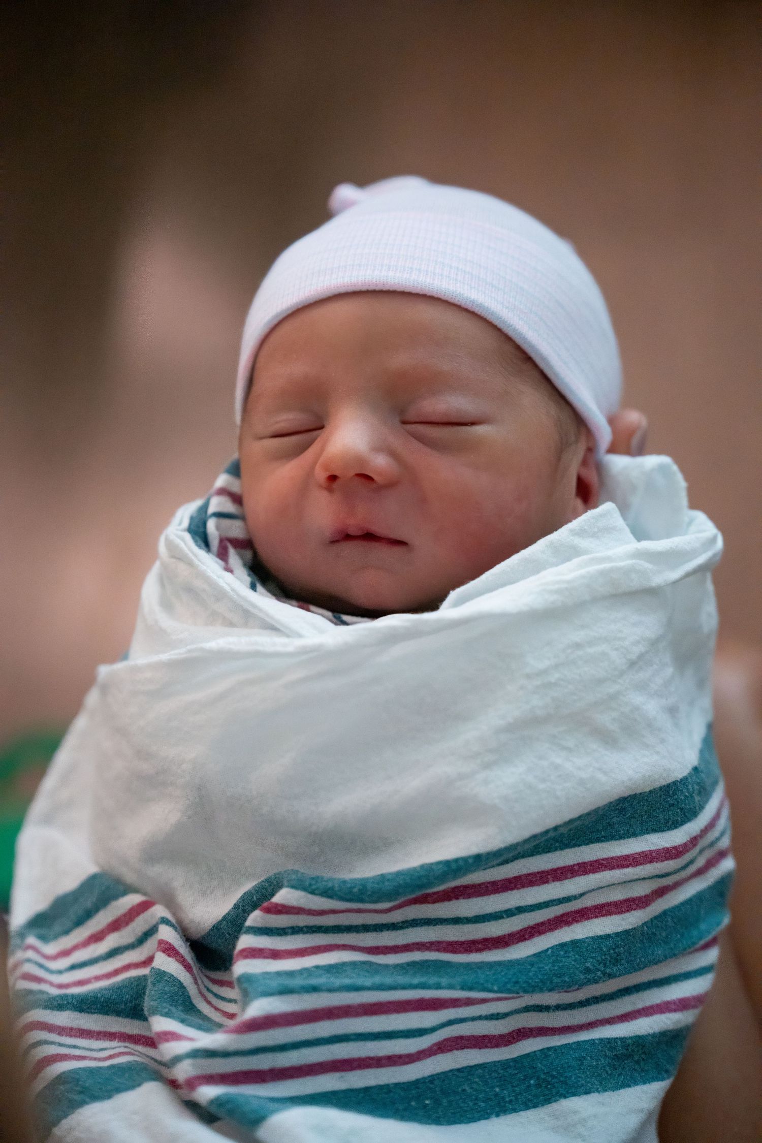 Close-up newborn portrait of baby swaddled in hospital blanket with white cap