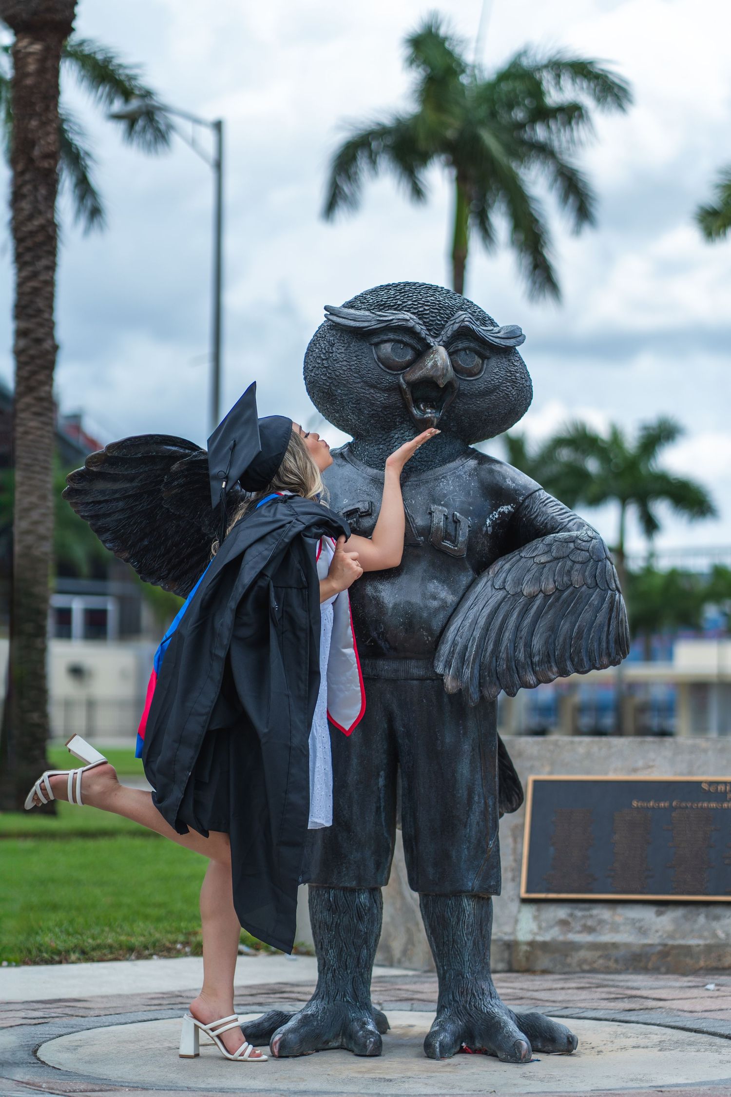 Florida Atlantic University graduate kisses the FAU owl statue during a fun graduation photo session in Boca Raton, FL.