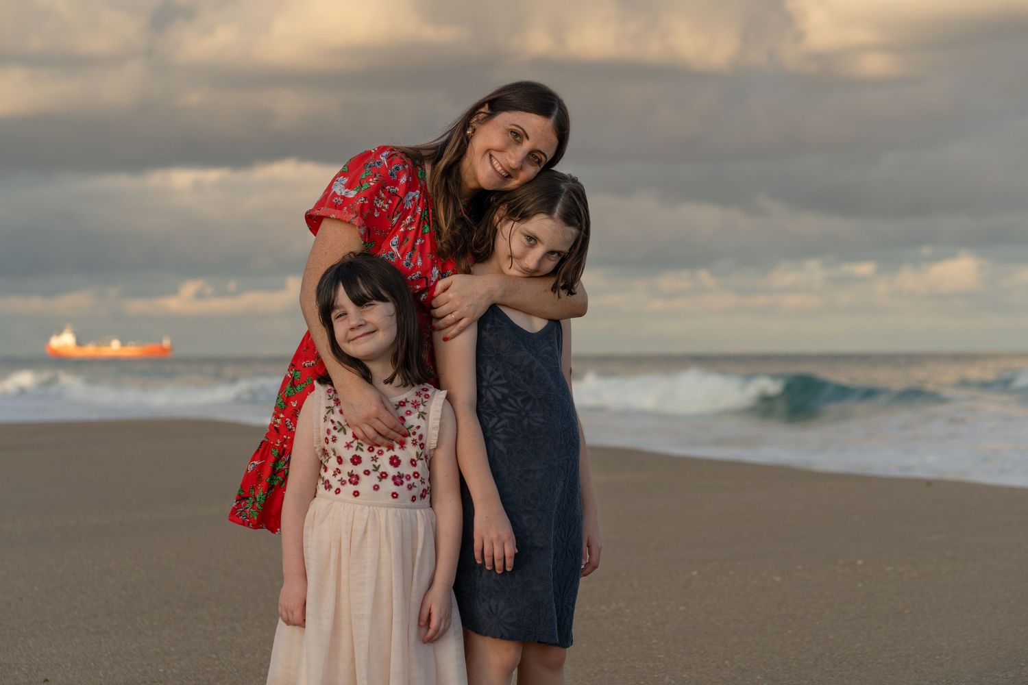 Mother-daughters beach portrait in Palm Beach, FL – joyful moment embracing on the sand with waves in the background.