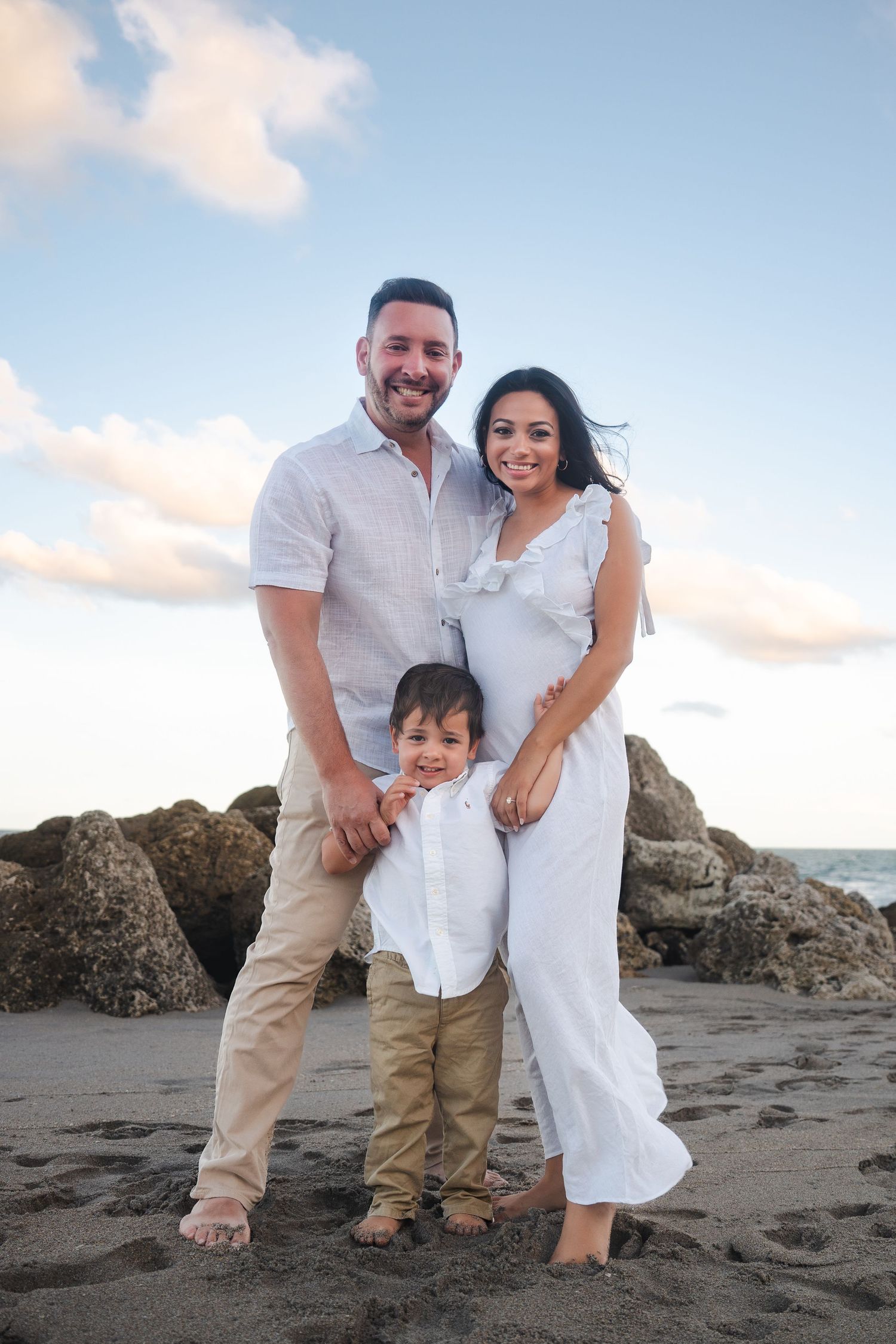 Family pregnancy announcement portrait of an expecting couple and child standing together on the beach in Deerfield Beach.