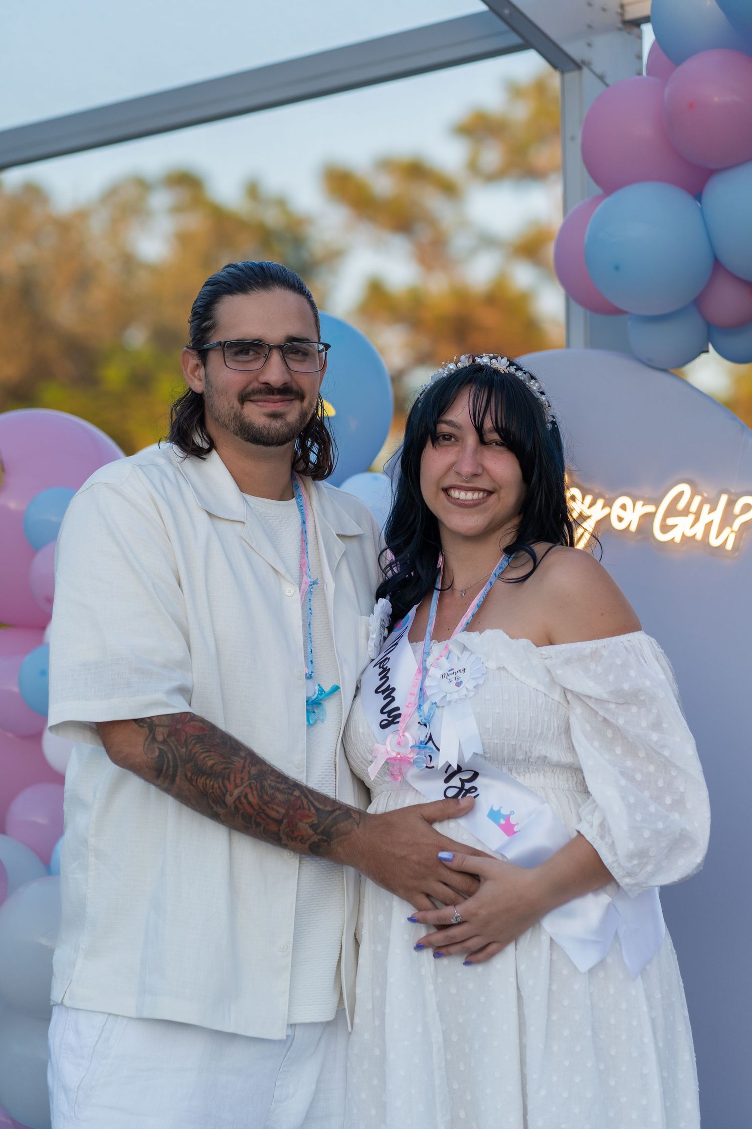 Expecting couple posing together under a pink and blue balloon arch during a South Florida gender reveal event.