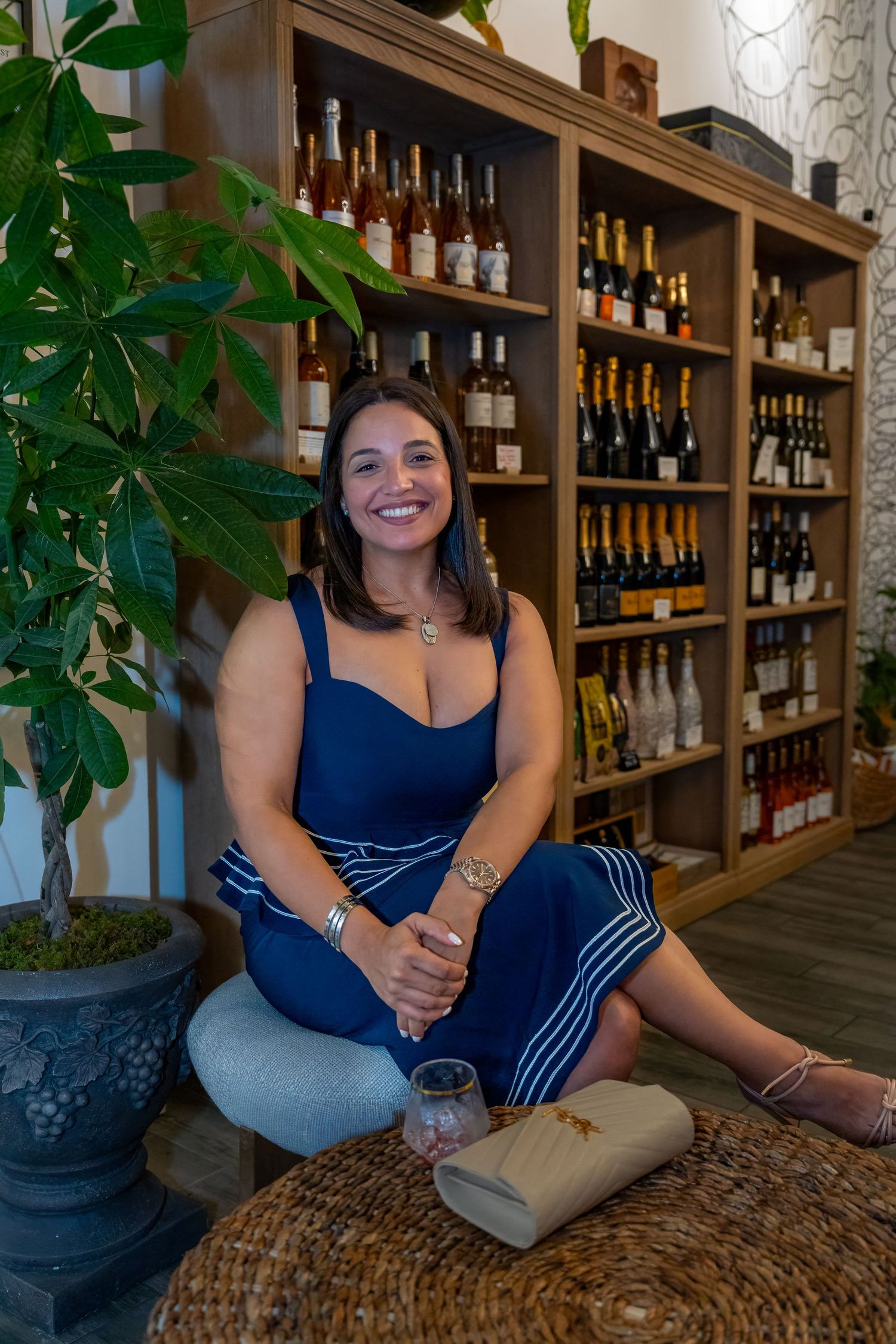 Portrait of a woman seated inside Bartolo’s Wine Bar & Cigar Shop surrounded by wine bottles during the grand opening.