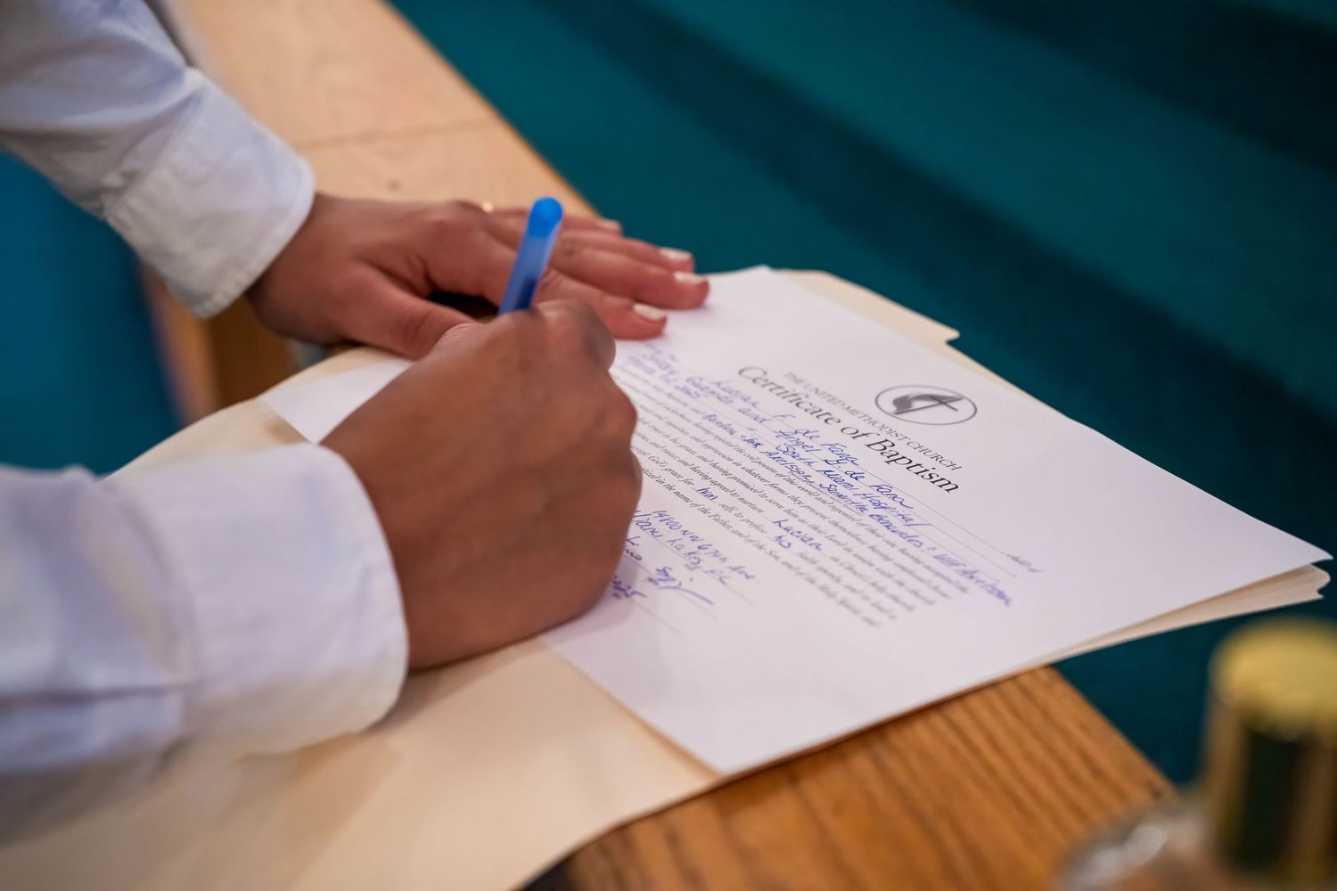 Close-up of hands signing baptism documents during a church ceremony, capturing meaningful details of a family baptism service.