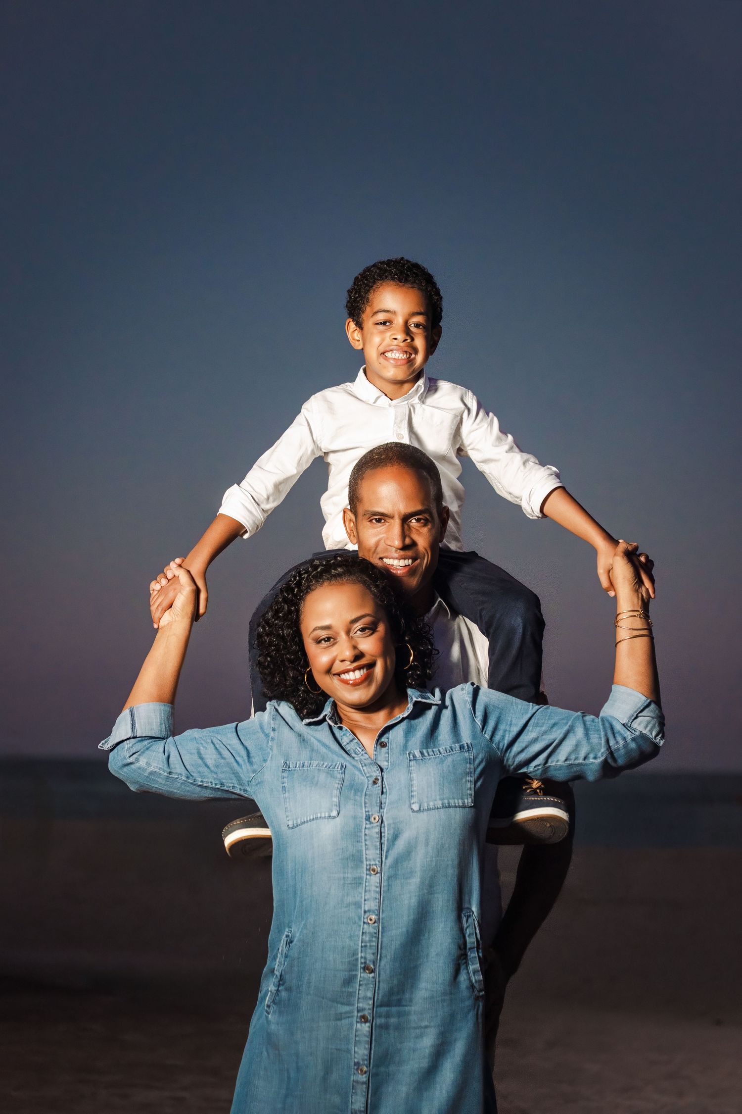 Child sitting on parent’s shoulders during a fun, candid family portrait session at dusk. Fort Lauderdale