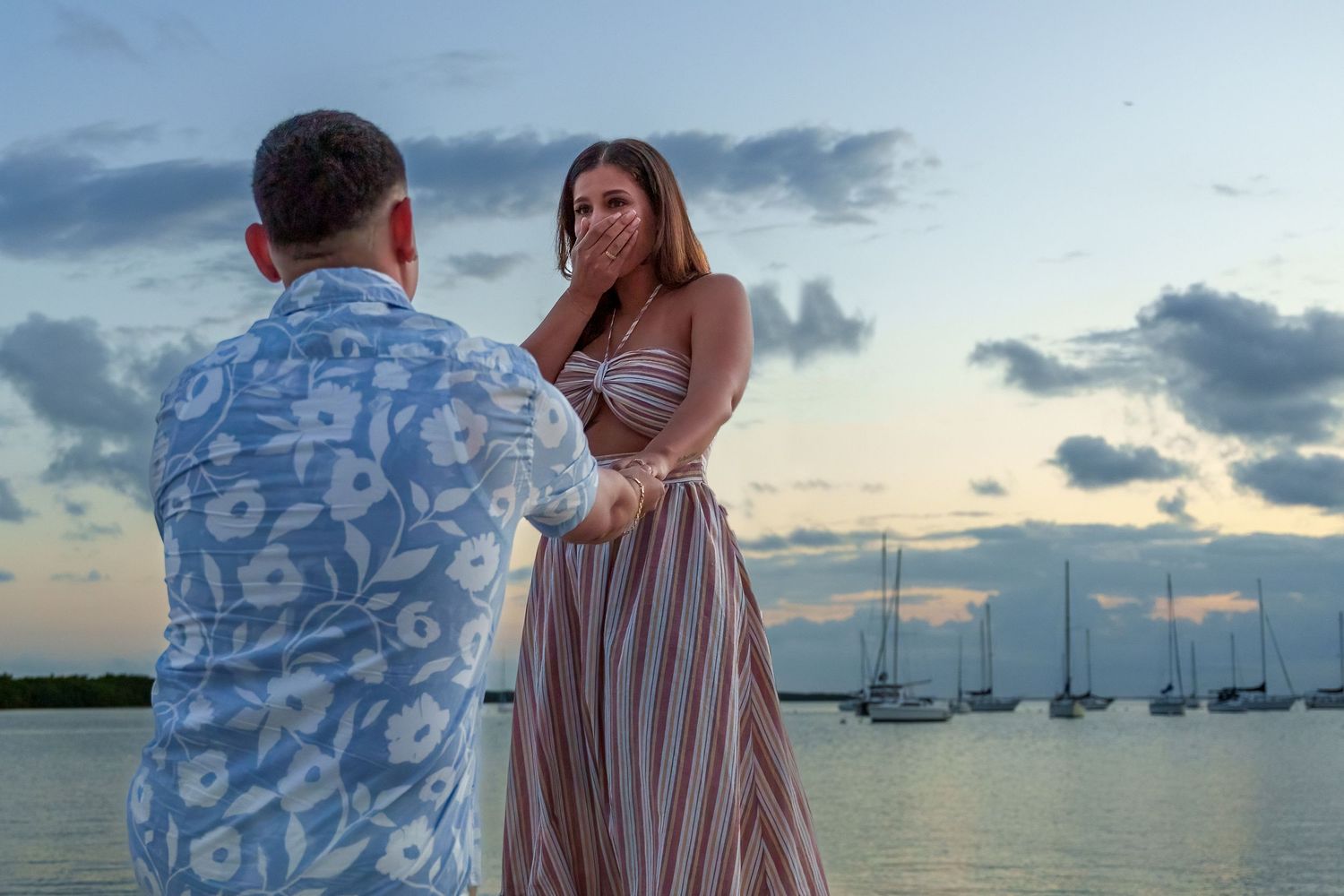 Couple holding hands at sunset during a proposal session in Key Biscayne with sailboats in the background.
