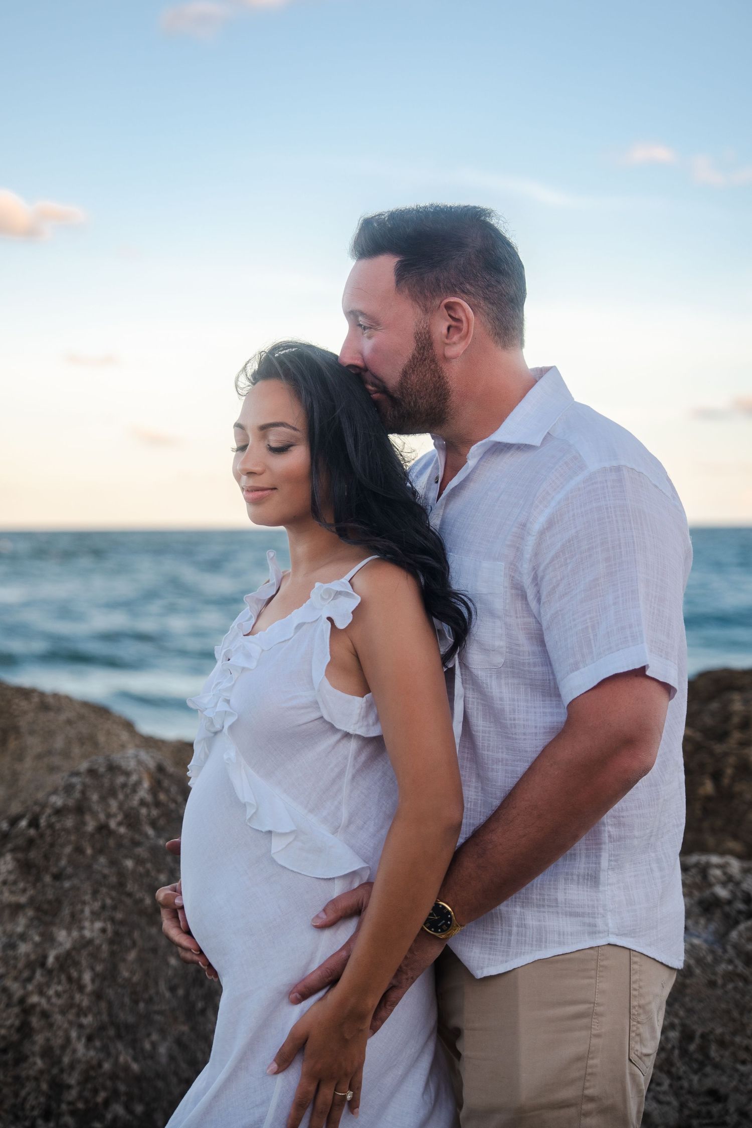 Soft maternity pregnancy announcement photo of an expecting couple embracing along the shoreline at Deerfield Beach.