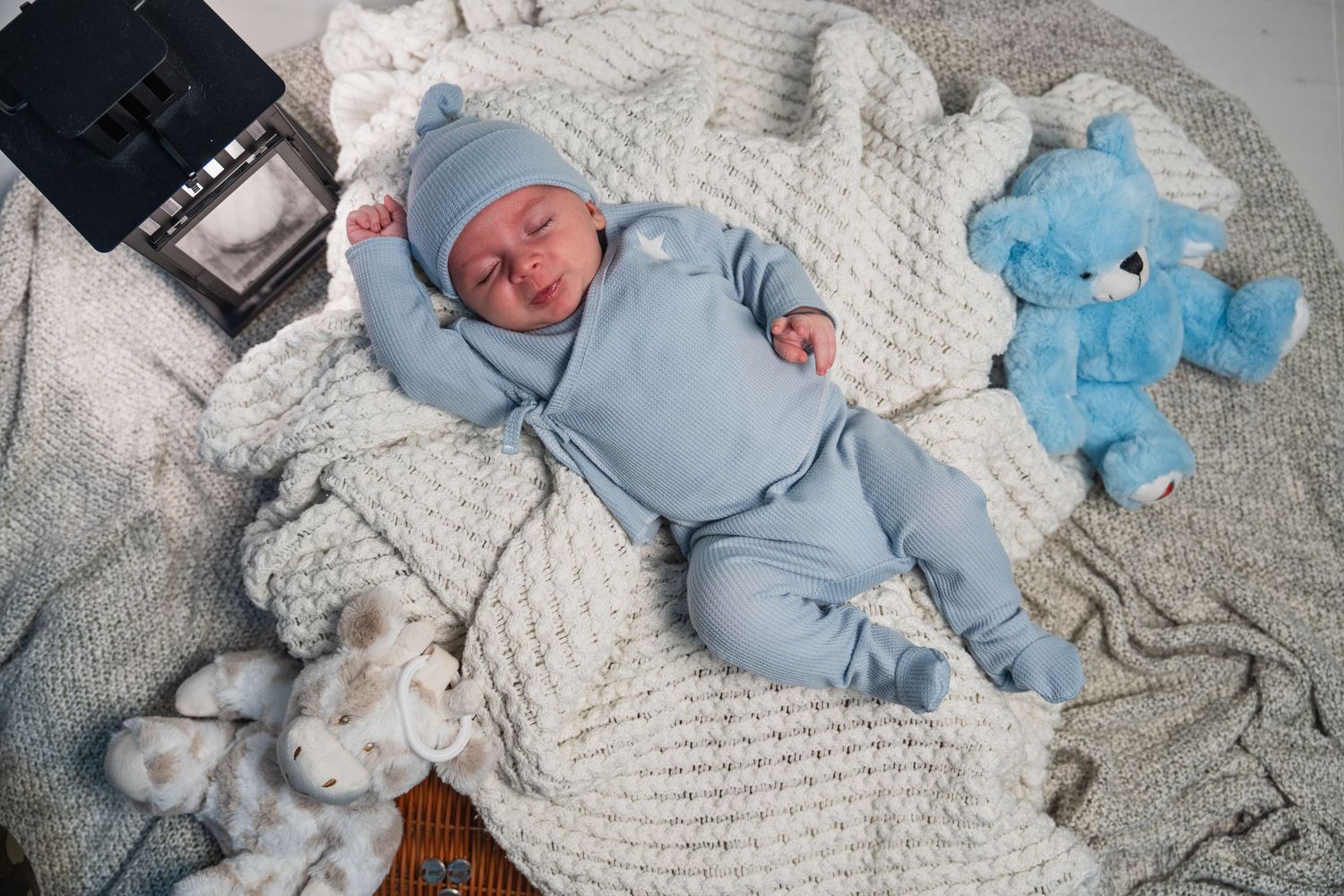 Newborn baby in blue outfit lying on blanket with plush toy during Miami session