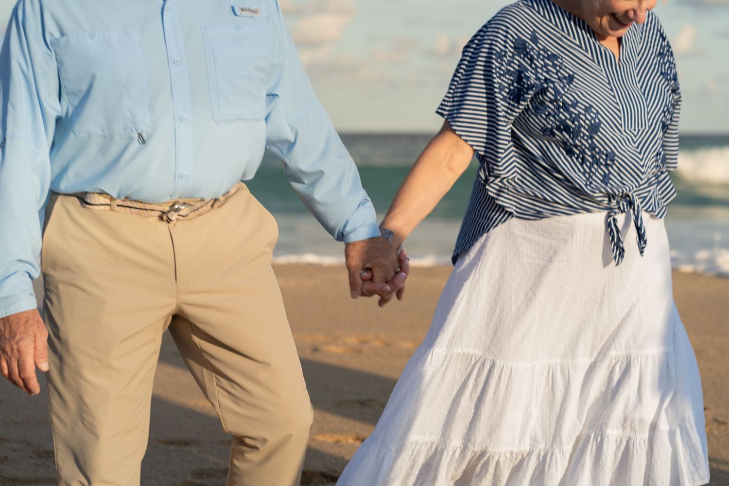 Senior couple walking hand-in-hand in Boynton Beach, FL – romantic golden hour stroll along the shoreline.