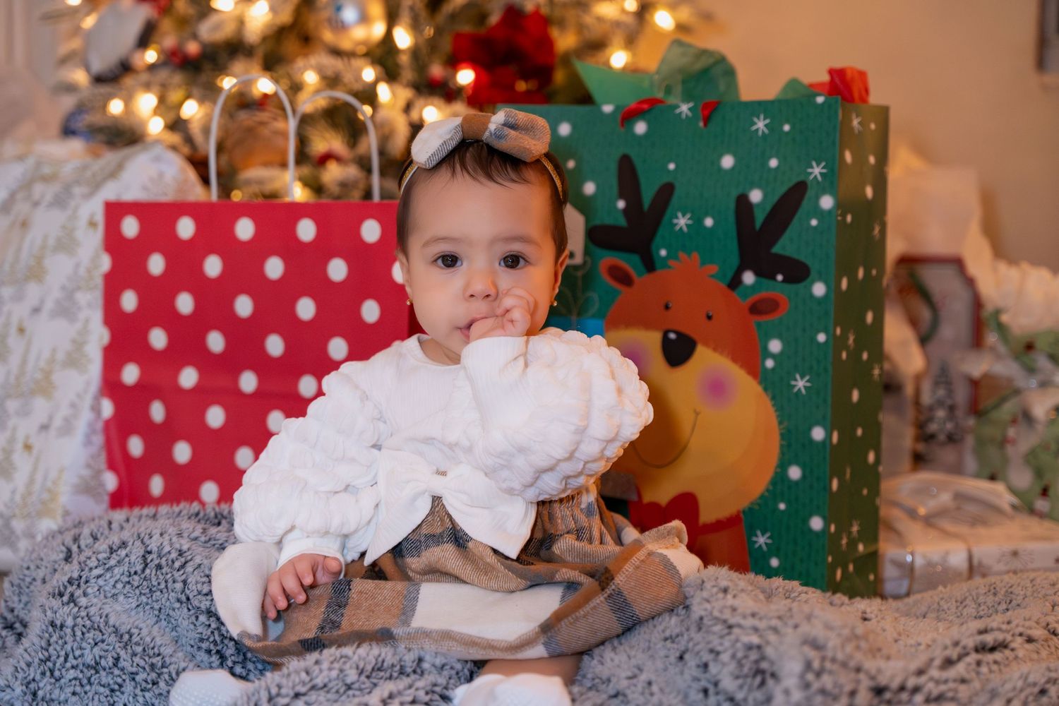 Adorable baby Christmas mini session in Delray Beach, FL – little one sitting by holiday gifts with twinkling tree lights.