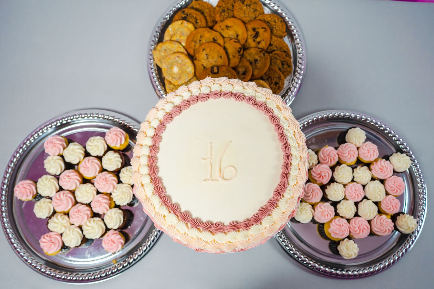 Overhead shot of a pink Sweet 16 cake surrounded by cookies and cupcakes at a birthday party. Event Photography