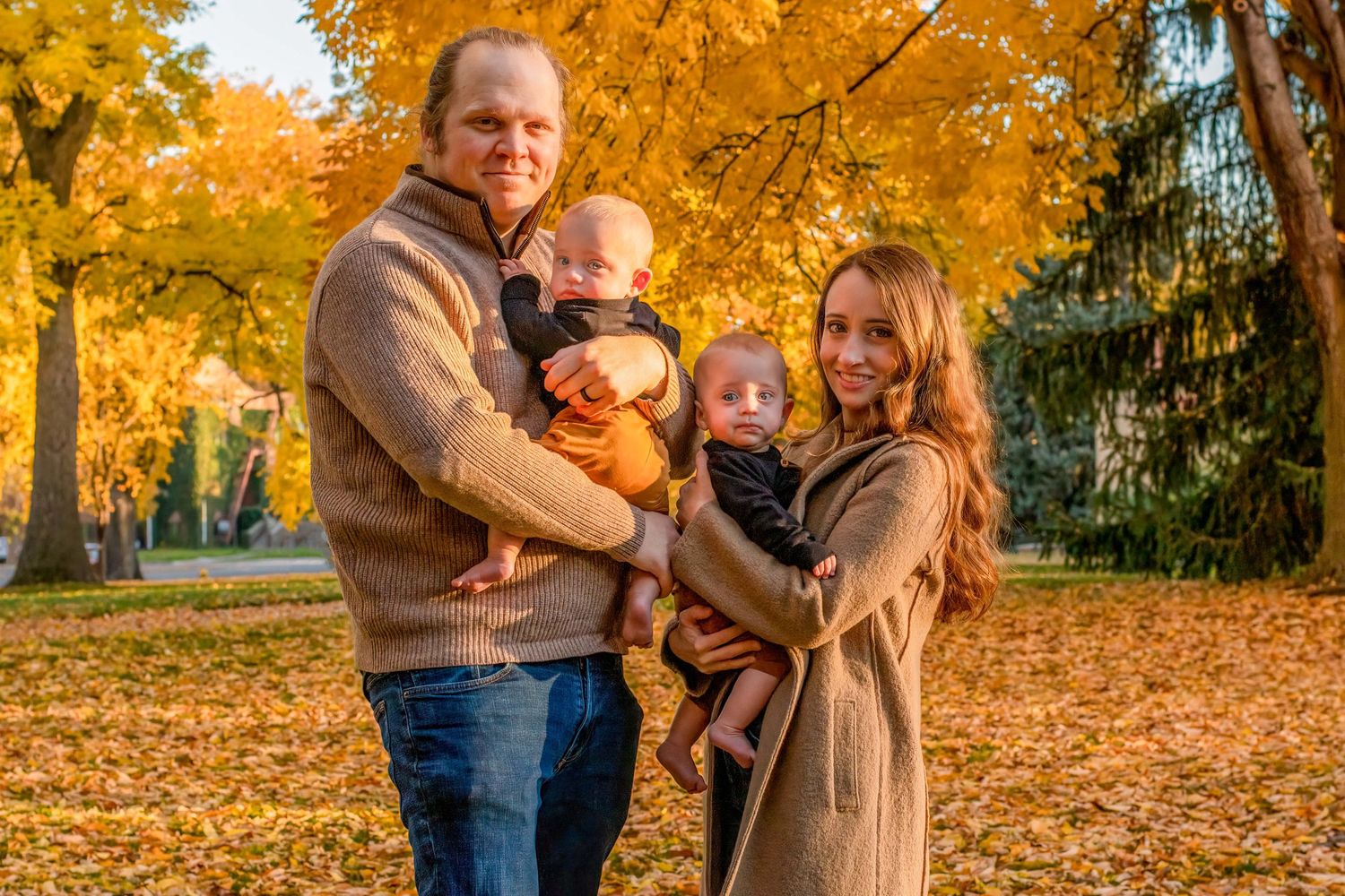 Fall family portrait in Boulder, CO – parents holding their twins under golden autumn leaves in a scenic park.