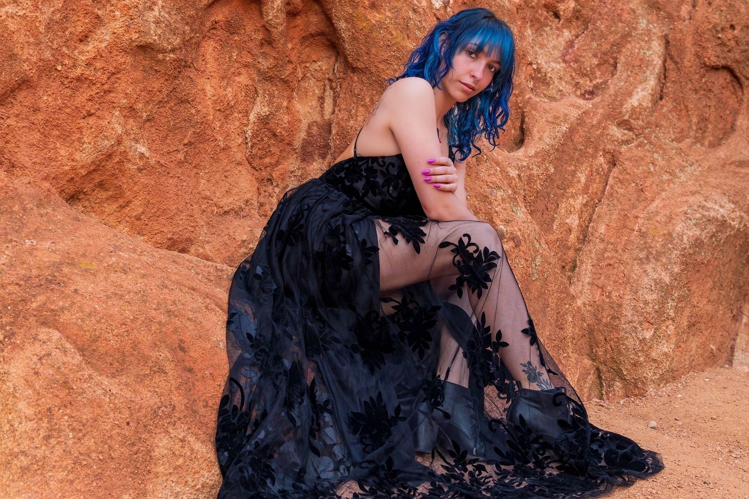 Mystical blue-haired woman in a black lace dress poses against the rugged red rock formations of Colorado.