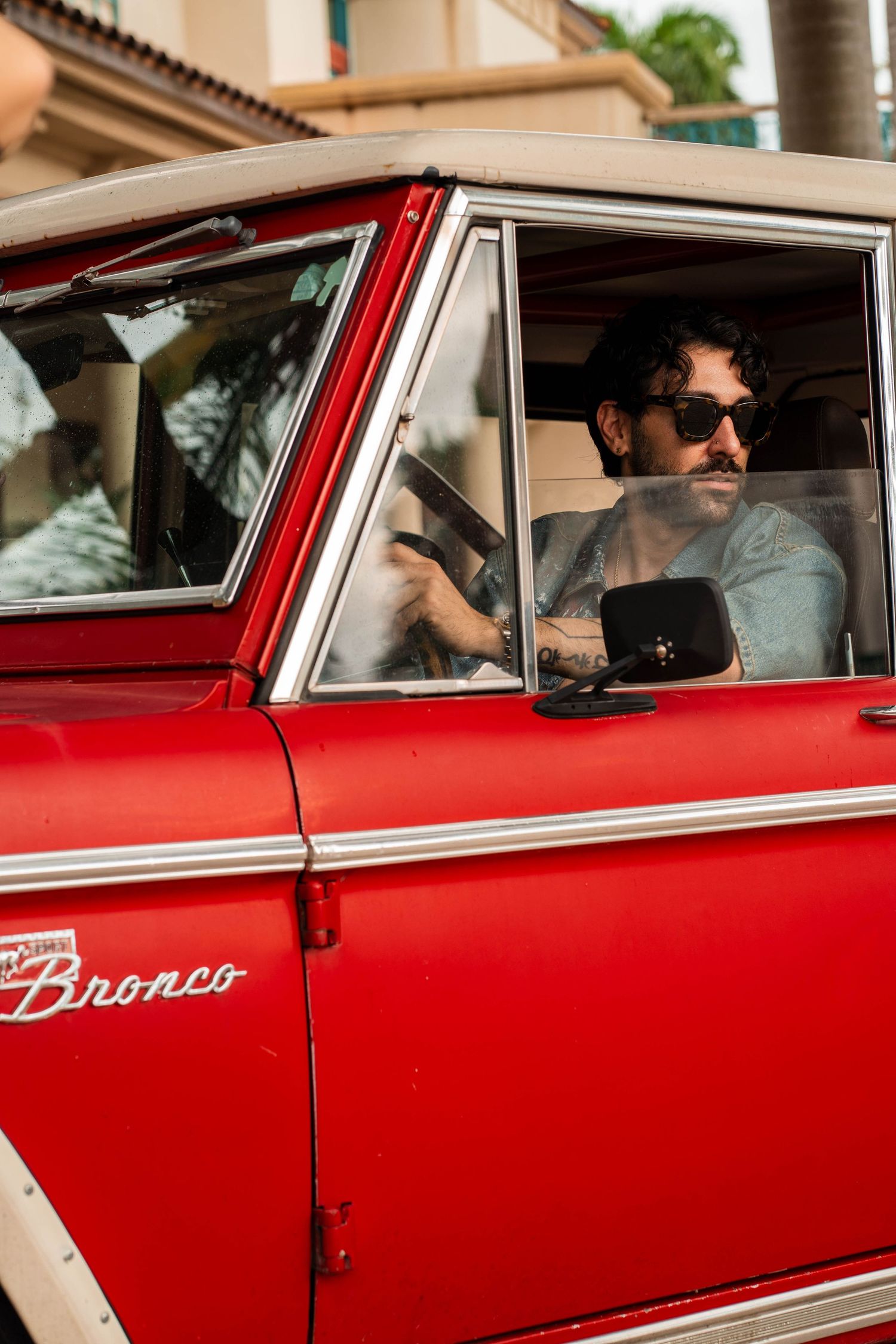 Classic automotive lifestyle shot in Fort Lauderdale, FL – driver framed through the window of a red Ford Bronco.
