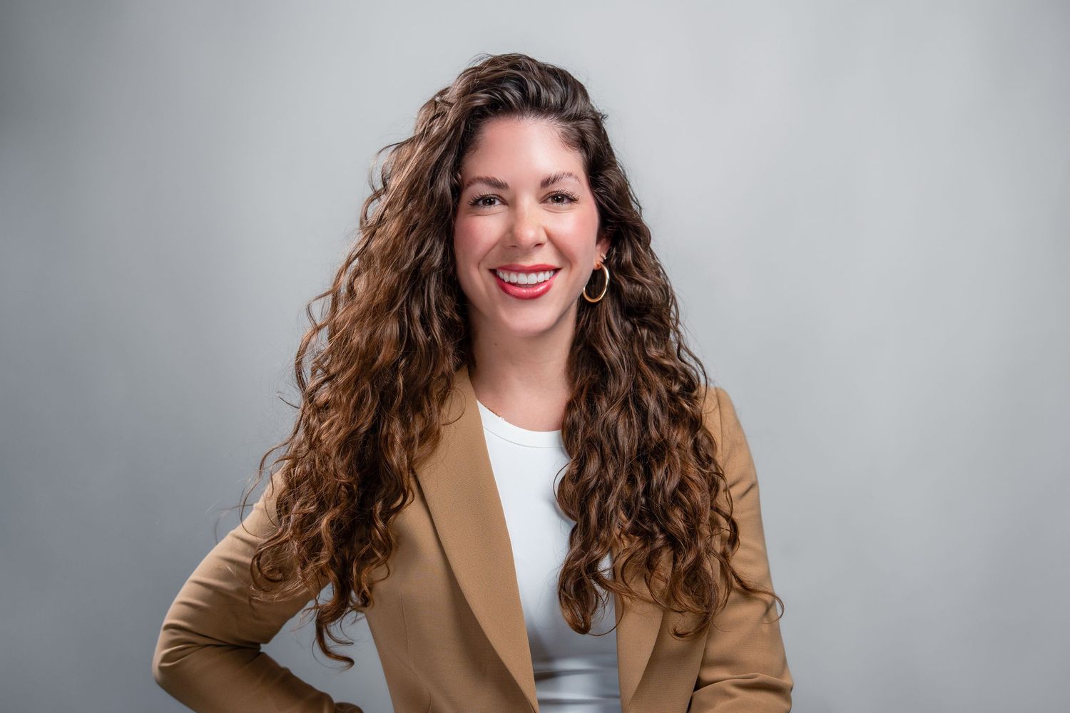 Professional woman in tan blazer smiling against gray studio background