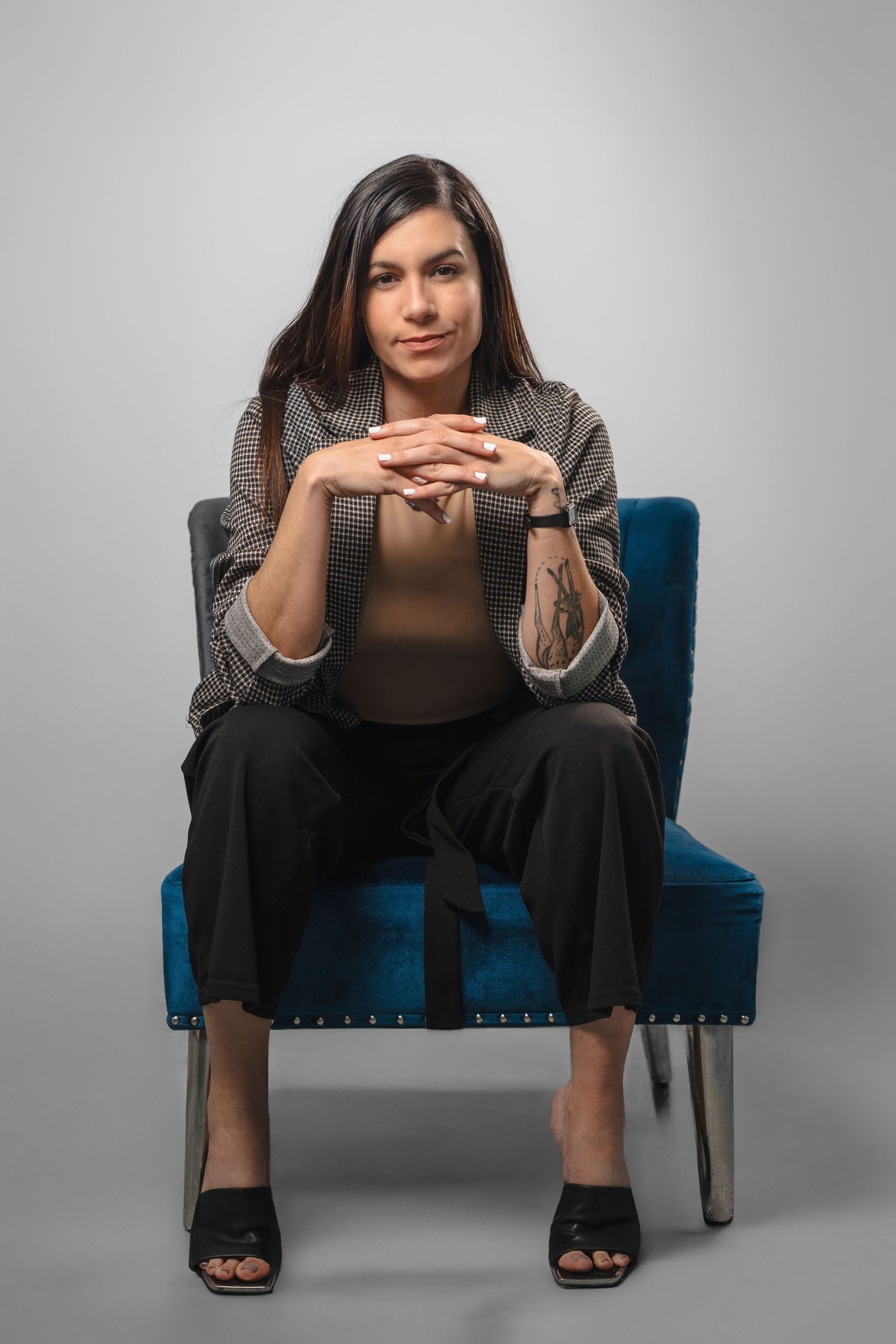 Stylish woman seated with hands folded in front of her during a professional portrait session.