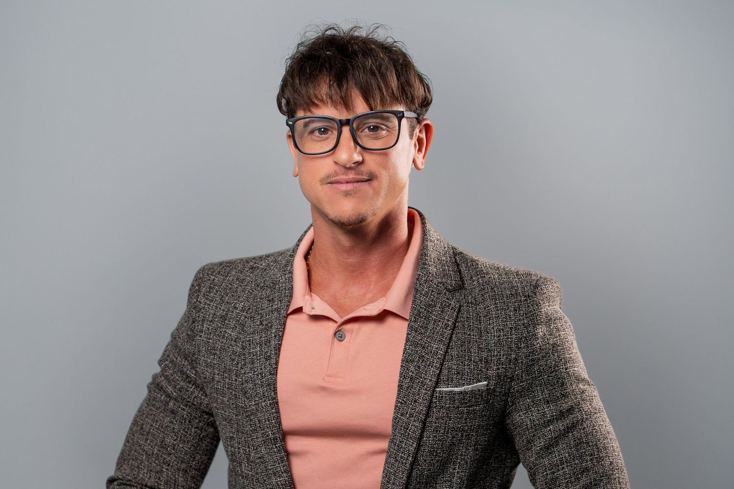 Confident headshot of a man in a speckled blazer and pink polo shirt for a business portrait.