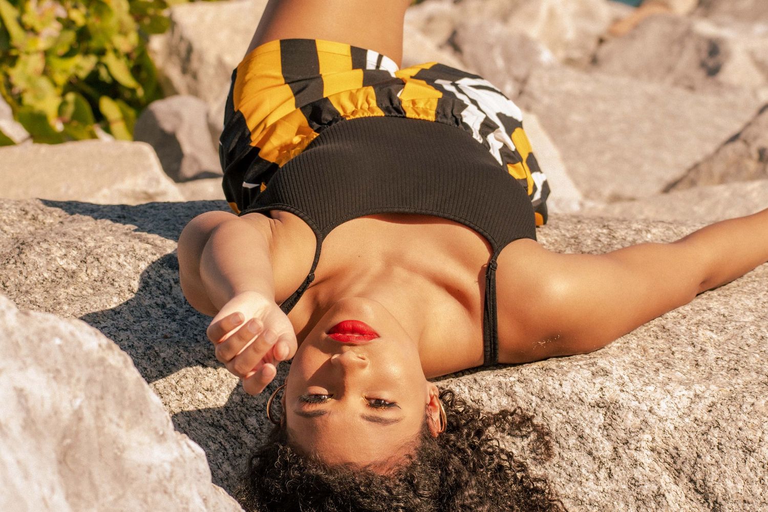 Sun-kissed beachside portrait of a woman lounging on rocks, embracing the golden hour glow in a bold patterned outfit. Haulover Beach FL