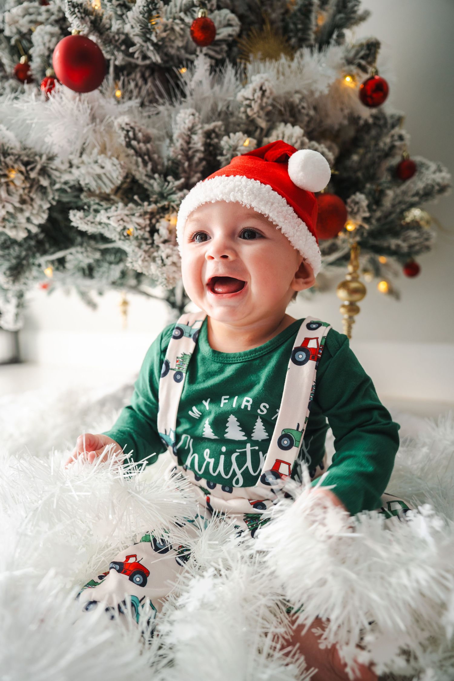 Baby sitting in front of a decorated Christmas tree during a holiday portrait session.