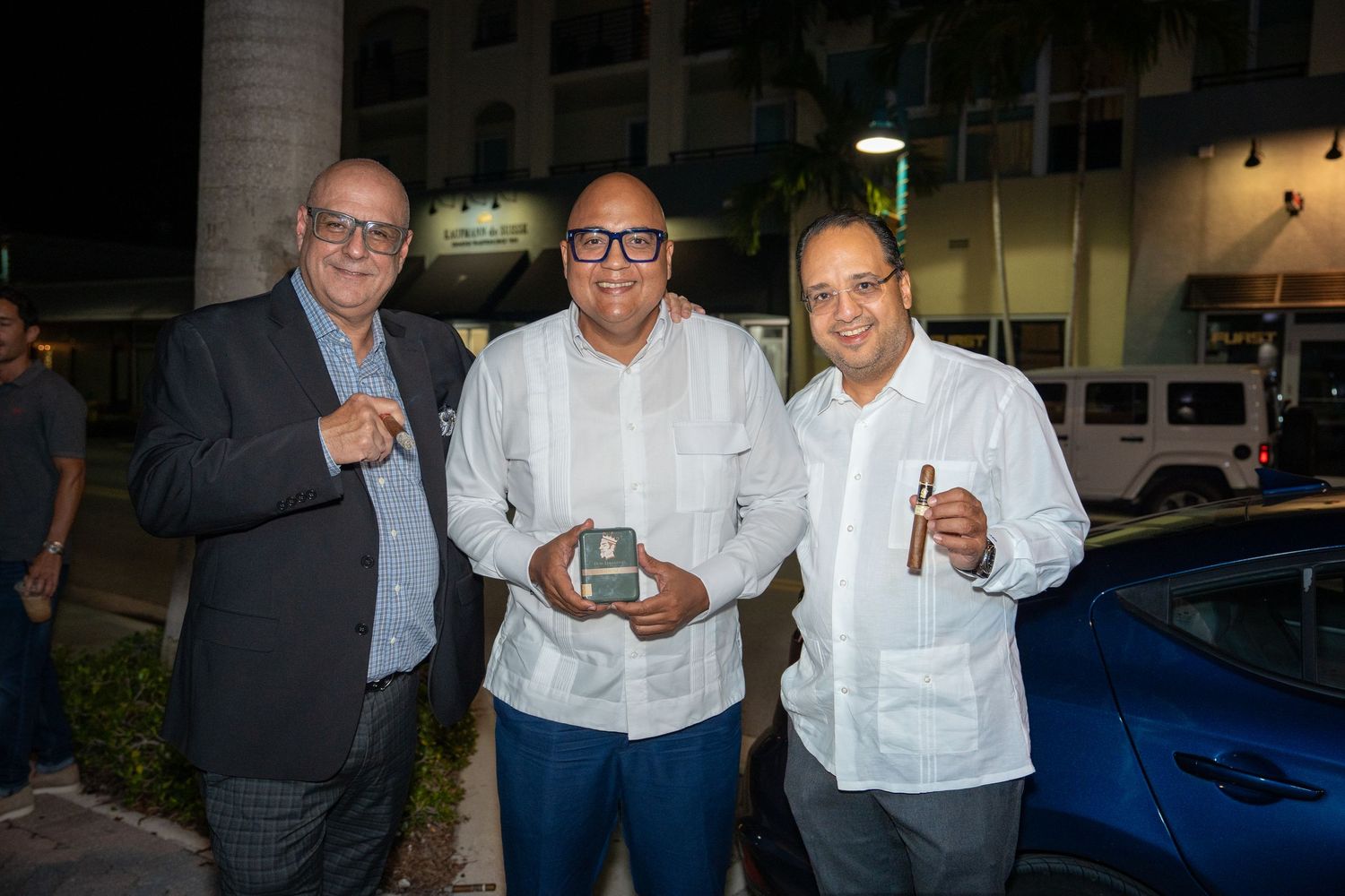 Three men smiling and posing together outside Bartolo’s Wine Bar & Cigar Shop during the grand opening celebration