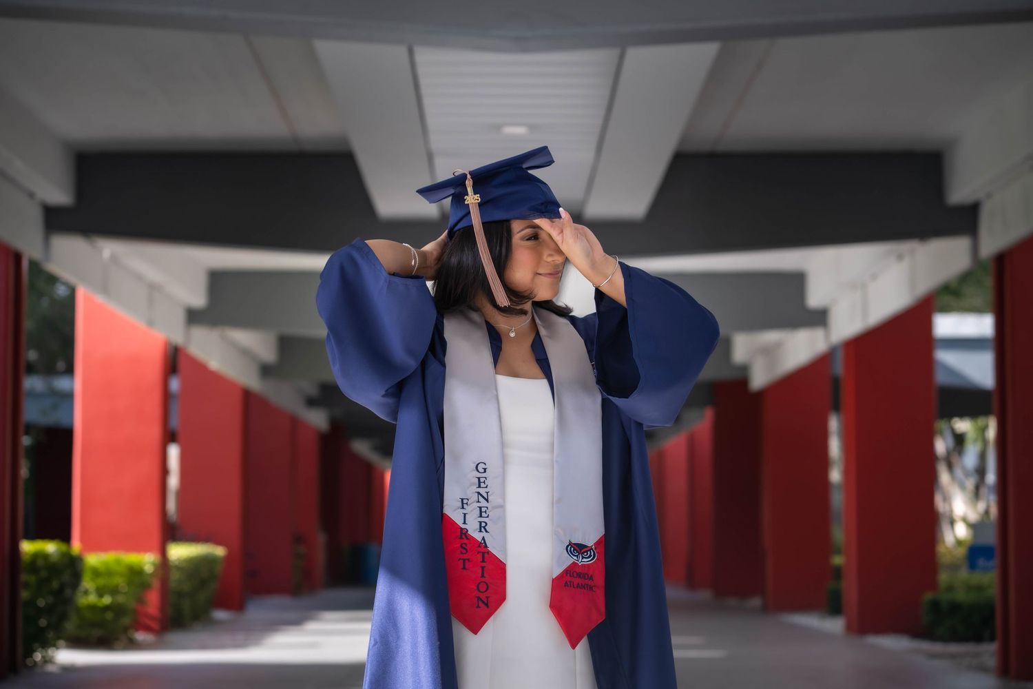 Graduation portrait of FAU student adjusting cap under archway on campus