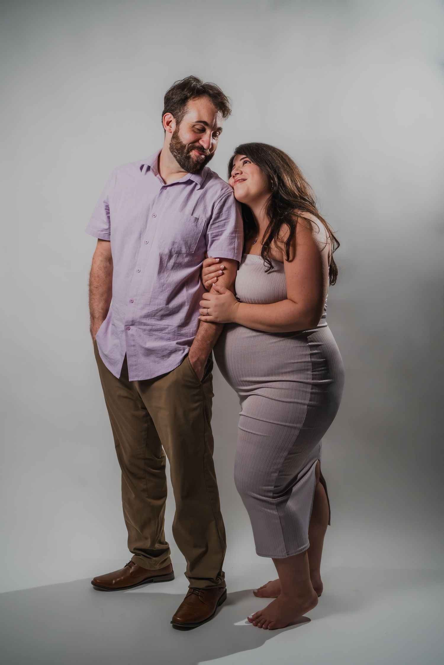 Studio maternity photo of expectant mother smiling while partner kisses her cheek