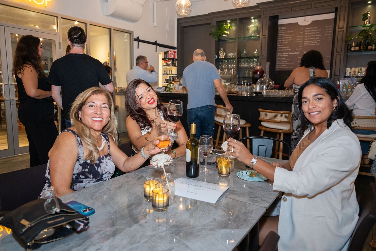 Group of women seated at a table enjoying drinks inside Bartolo’s Wine Bar & Cigar Shop during the grand opening.