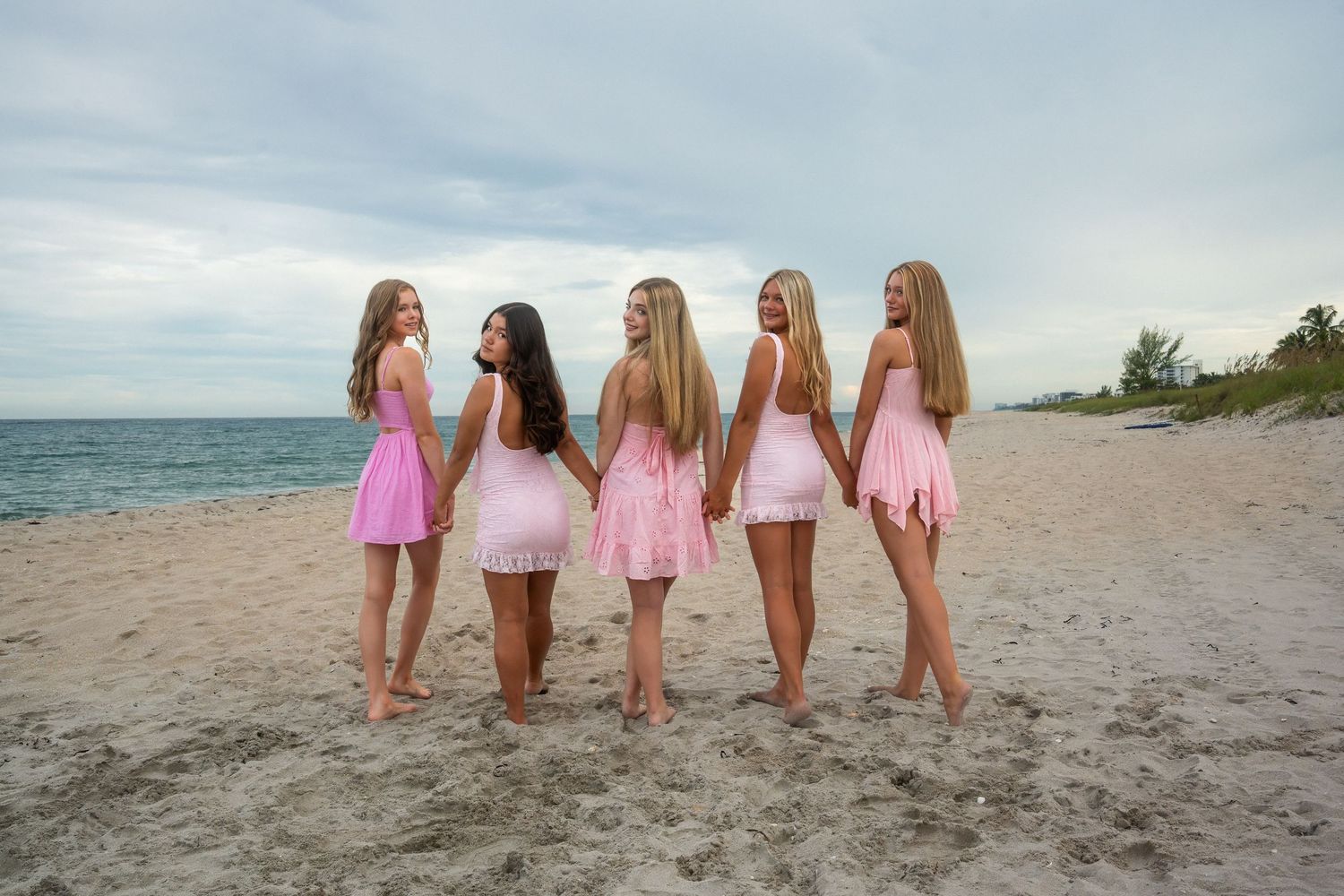 Beach portrait of a cheer squad walking along the shoreline in matching pink dresses during a South Florida photo session.