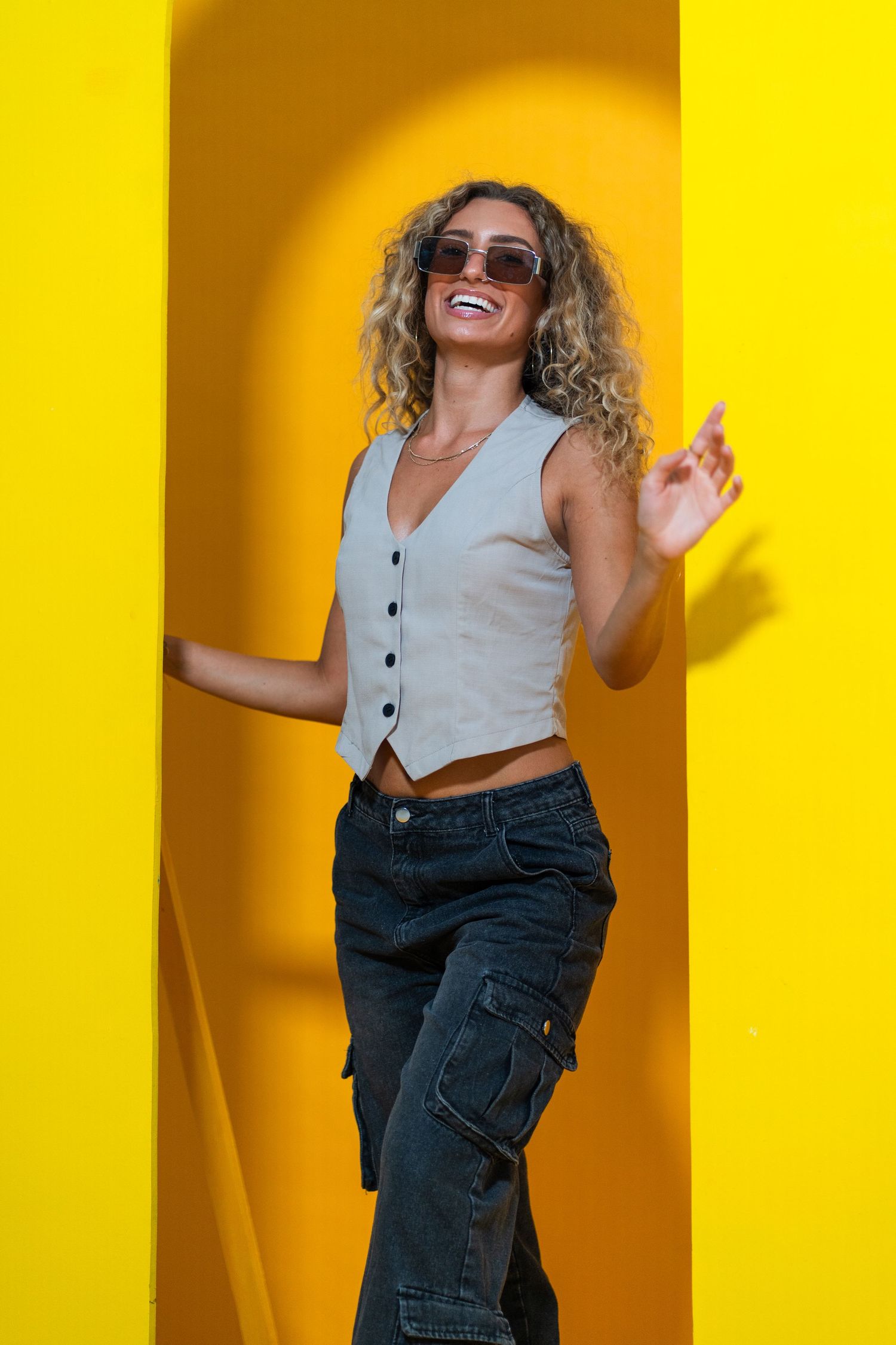 Editorial portrait at HGAB Studios – curly-haired woman in sunglasses leans against a bold yellow arch, exuding confidence.