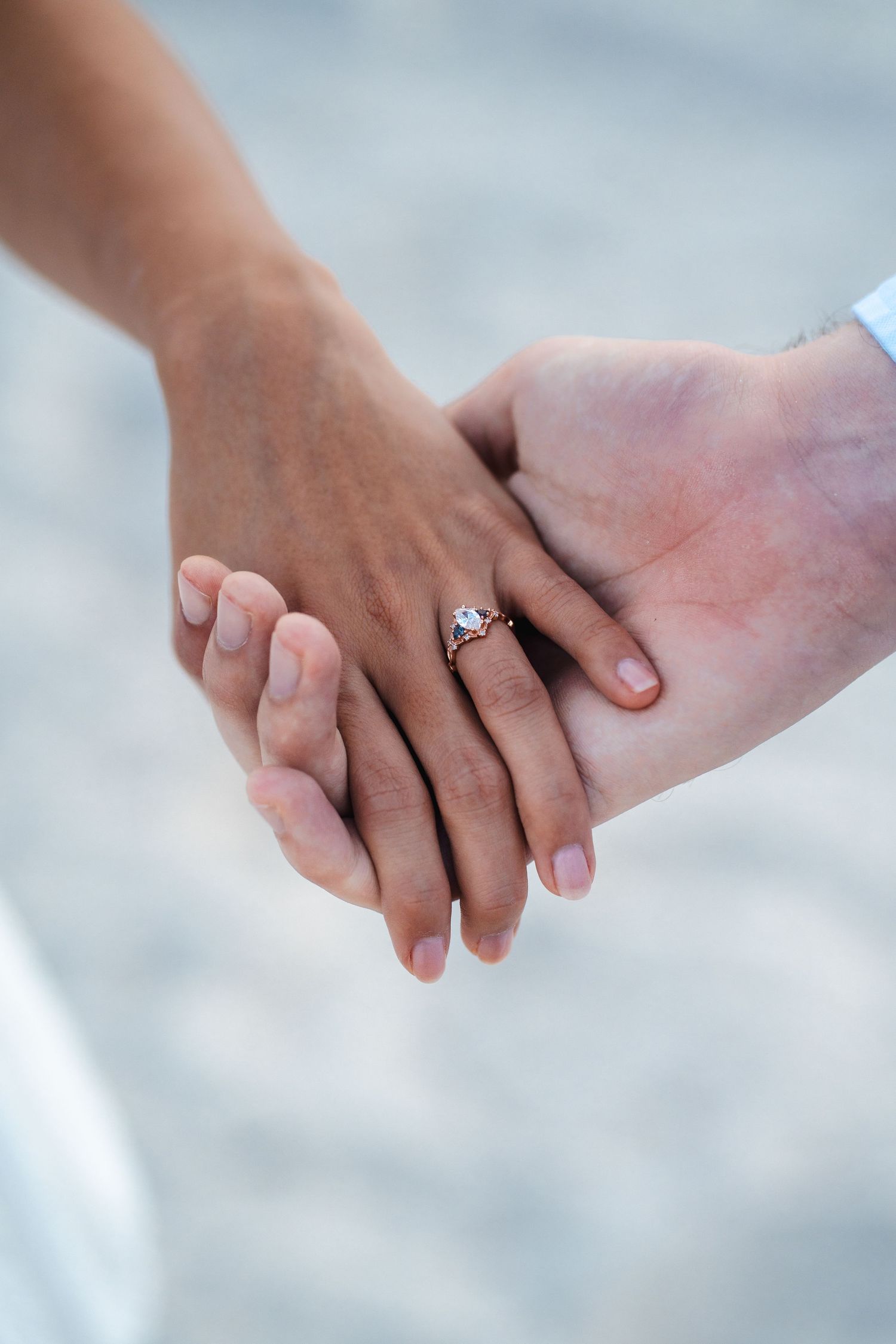 Hands holding together after an engagement, showing the ring against a soft beach background in South Florida.