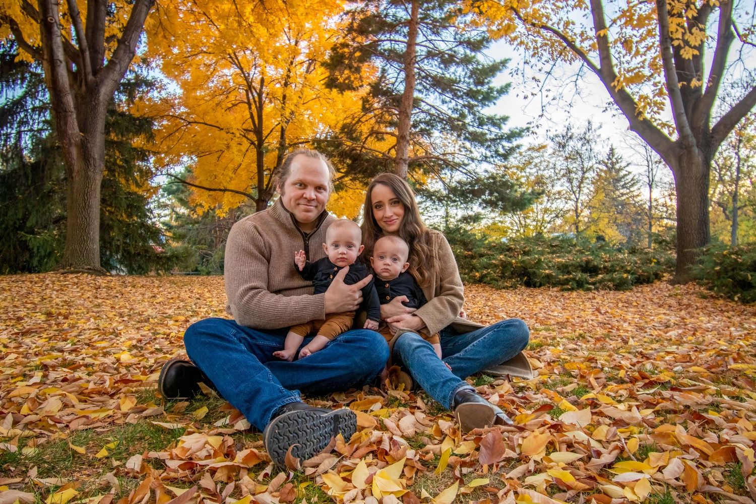 Cozy fall family portrait in Colorado Springs, CO – parents with newborn twins sitting on golden leaves in a scenic park.