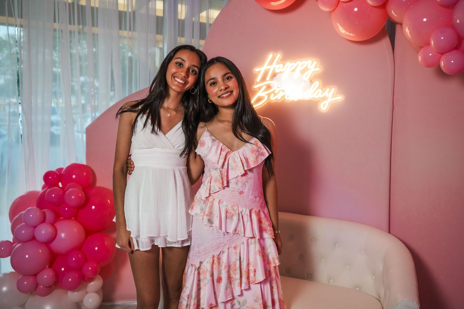 \Candid birthday portrait in front of pink neon sign and balloon garland during a celebration in Miami.
