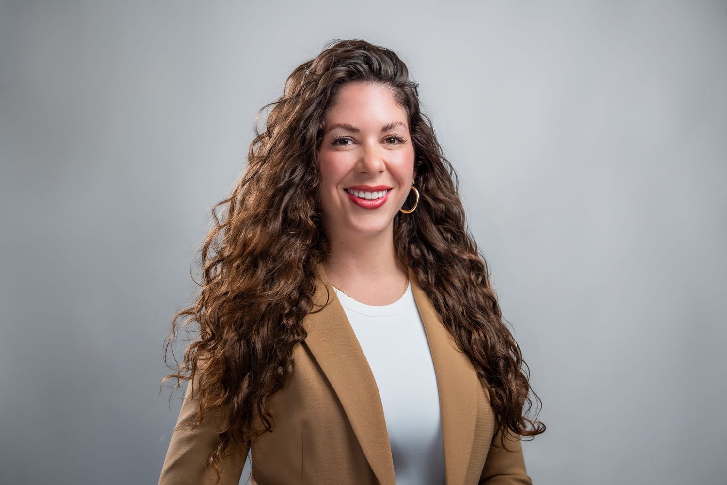 Woman with long curly hair in blazer smiling during studio headshot session