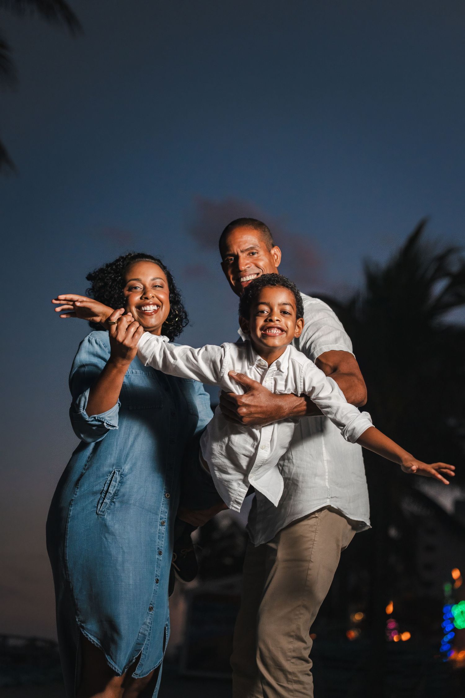 Playful family portrait at dusk with parents and child laughing together during a South Florida family session. Hollywood Beach