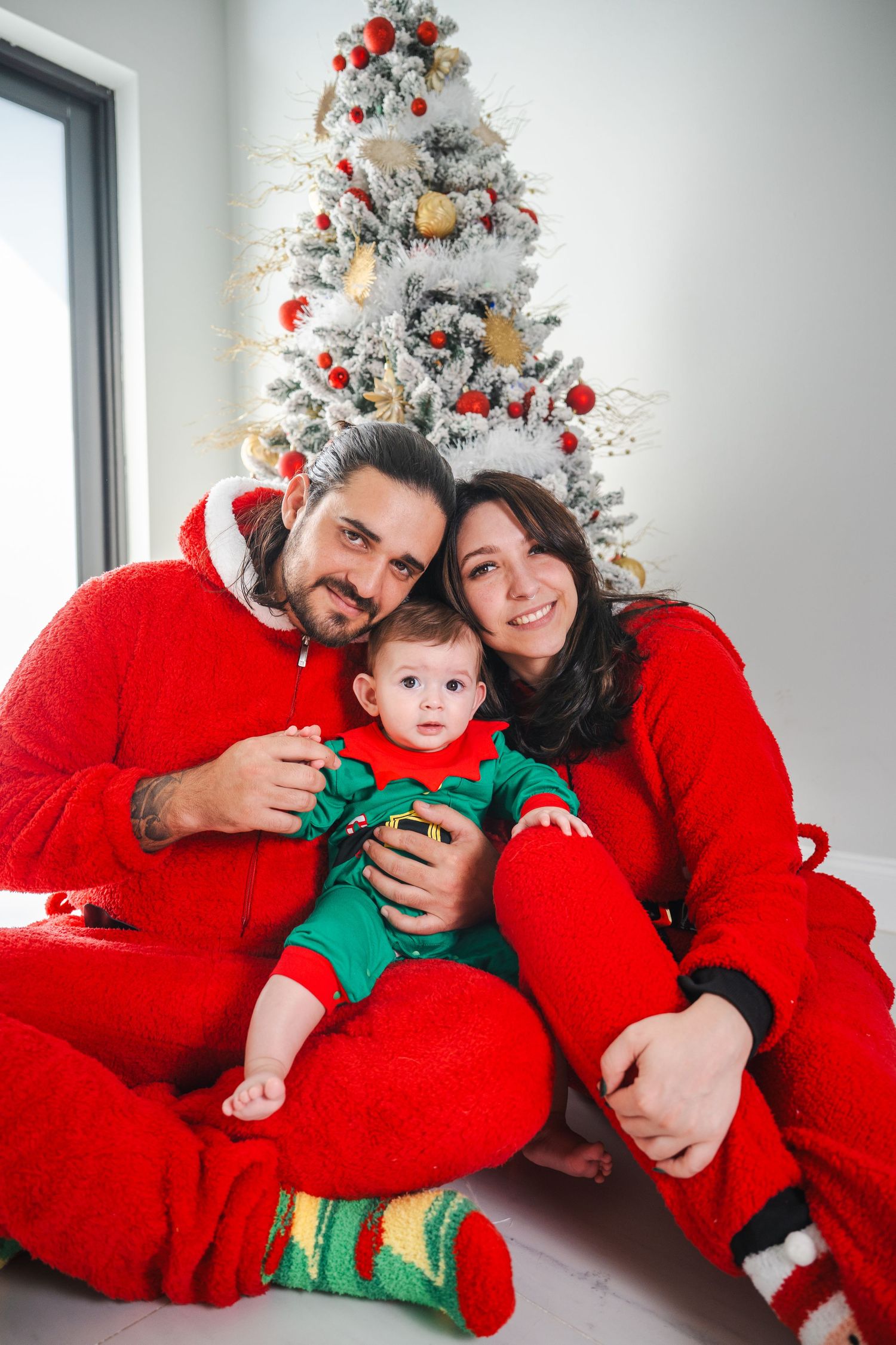 Family holiday portrait with parents and baby sitting together in matching Christmas outfits.