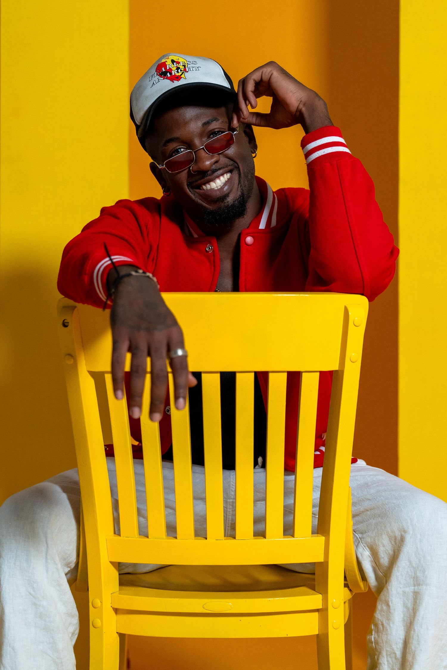 Energetic street-style portrait in Miami – stylish male model in red and white leans against a yellow chair, bringing a playful urban vibe.
