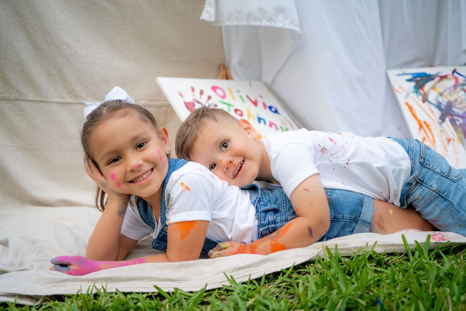 Siblings laying on their stomachs and smiling during a playful Mommy & Me painting session.