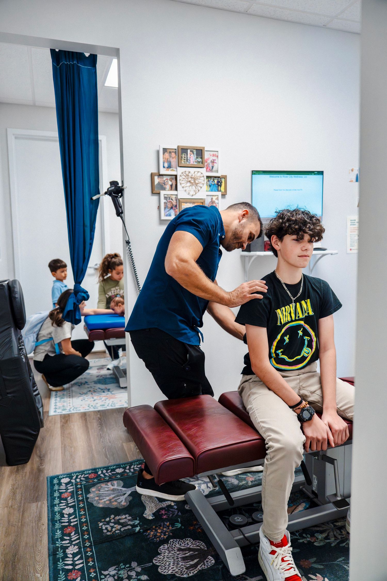 Chiropractor adjusting teenage patient’s shoulder on treatment table during in-clinic branding shoot