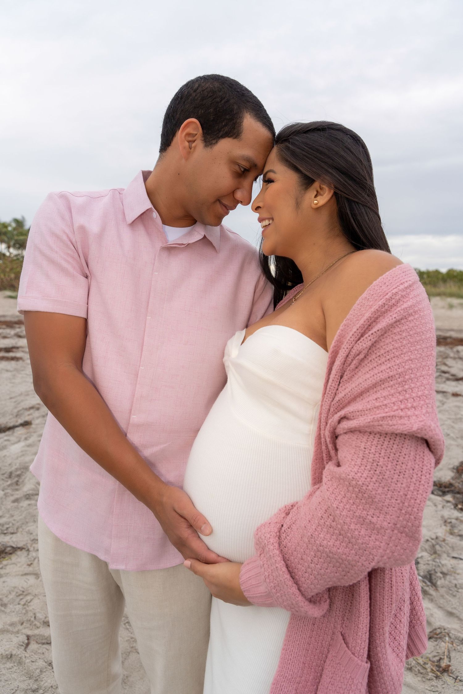 Romantic maternity session at Cape Florida Lighthouse, Key Biscayne, capturing an expecting couple embracing on the beach with soft neutral