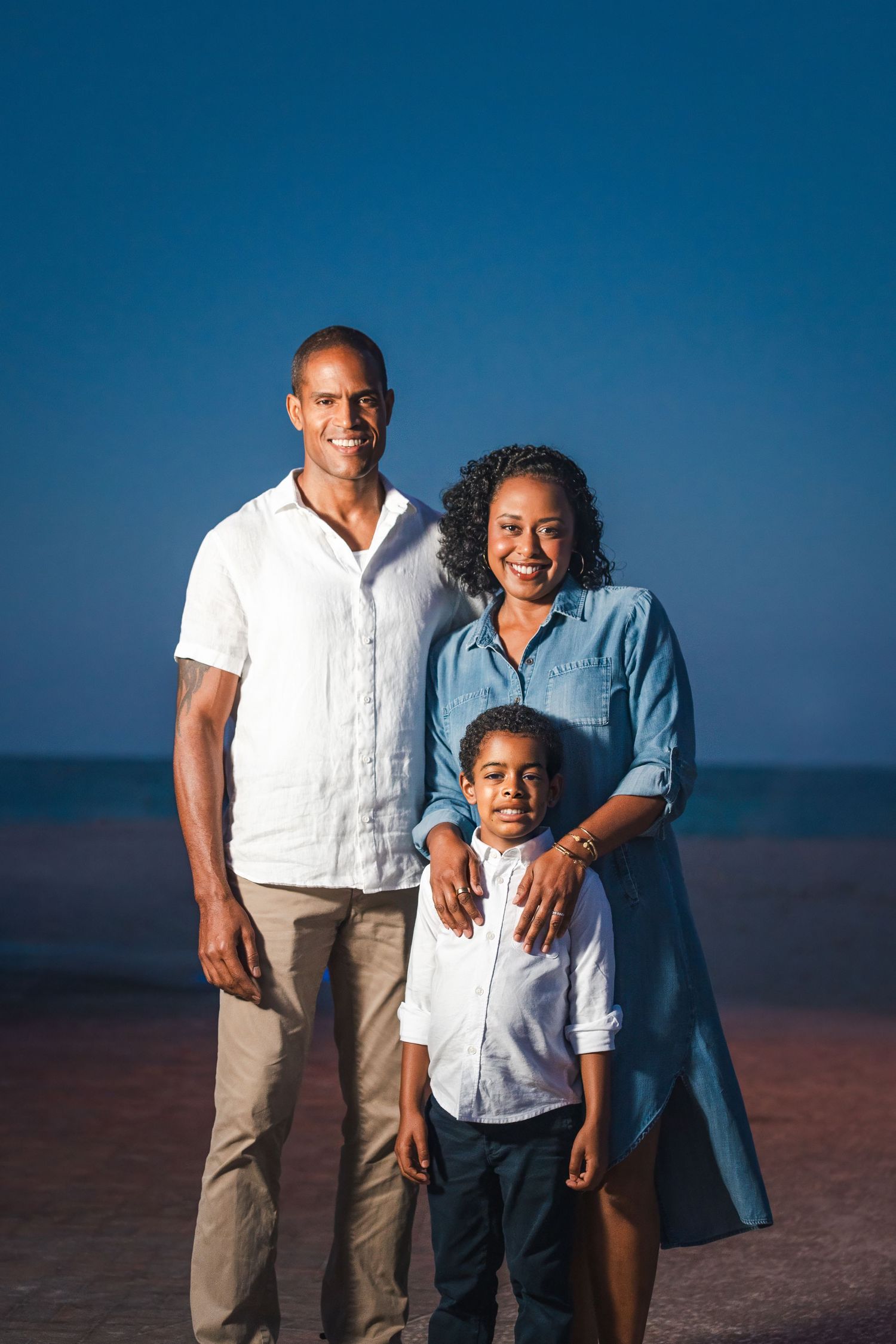 Family of three standing together at sunset, relaxed and natural family photography in South Florida.