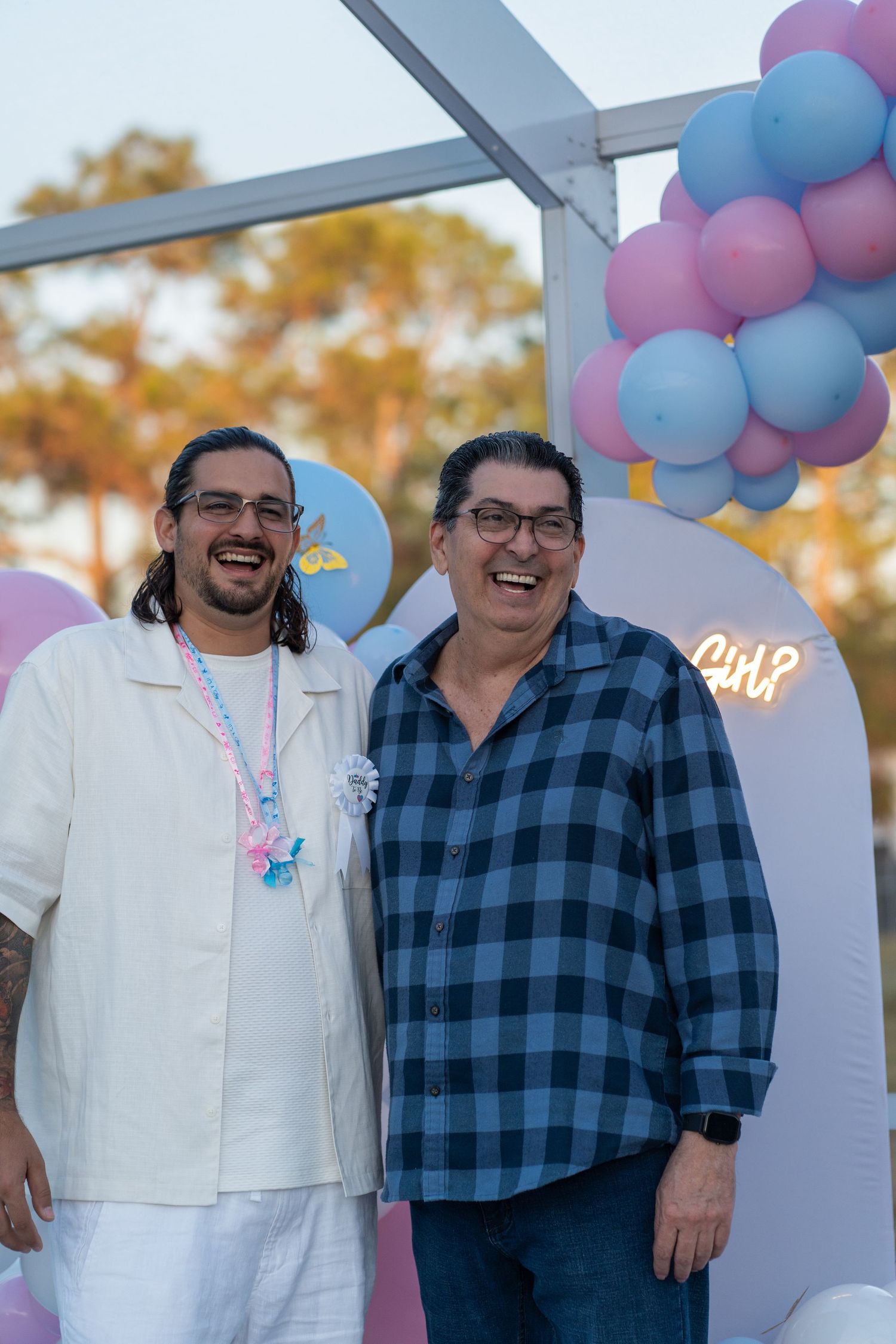 Father and son smiling together beneath a pink and blue balloon arch at a South Florida gender reveal celebration.