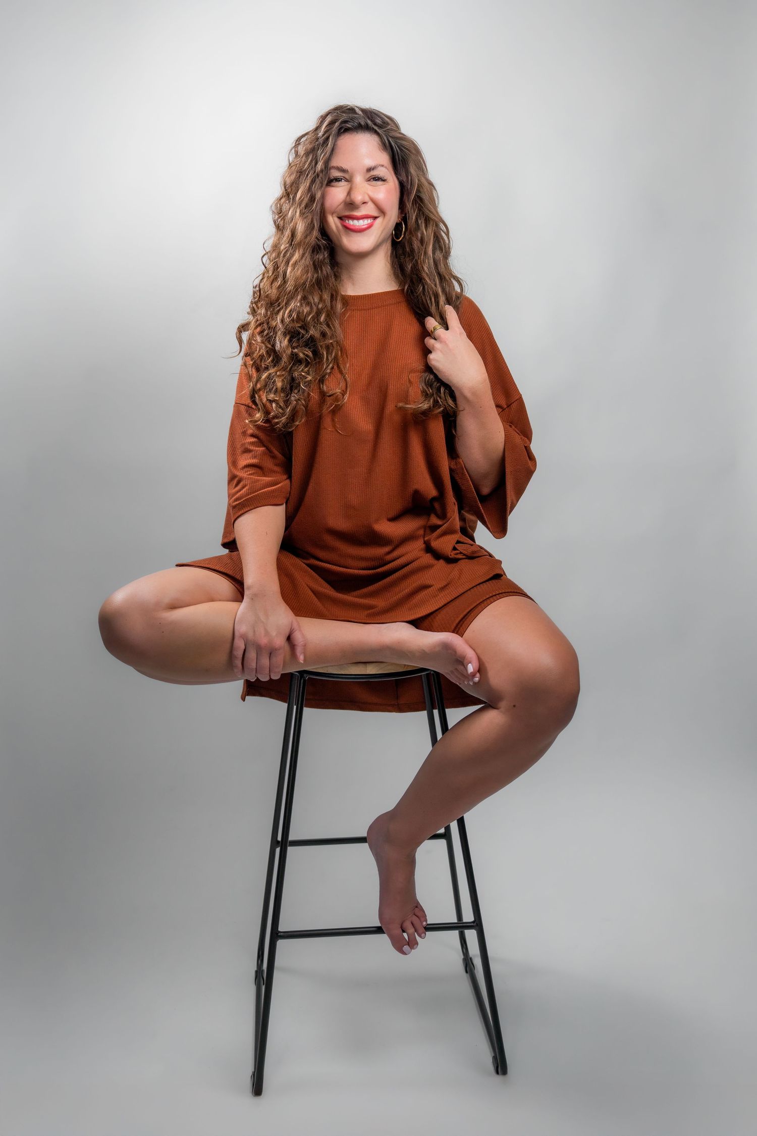 Studio portrait of a woman sitting on a stool against a neutral backdrop during a professional headshot session in South Florida.