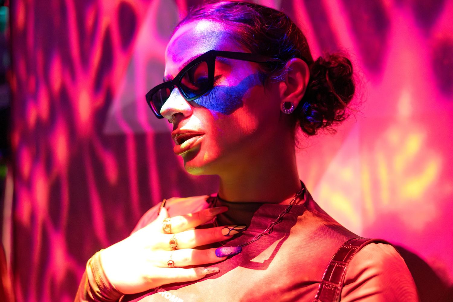 Vibrant neon-lit portrait of a stylish woman in sunglasses, bathed in bold pink and purple lighting at an urban creative space.