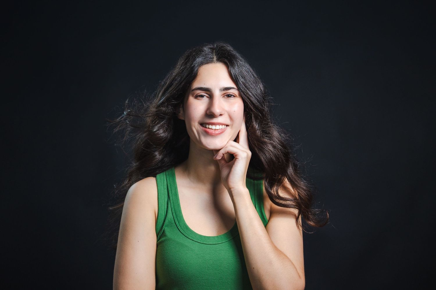 Actress with long dark hair posing against dark background during studio headshot session