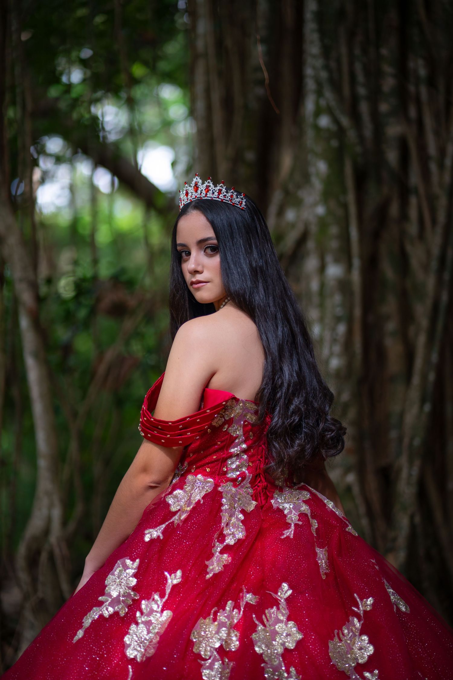 Glamorous teen portrait in a red gown with long train flowing behind her on a forest path.