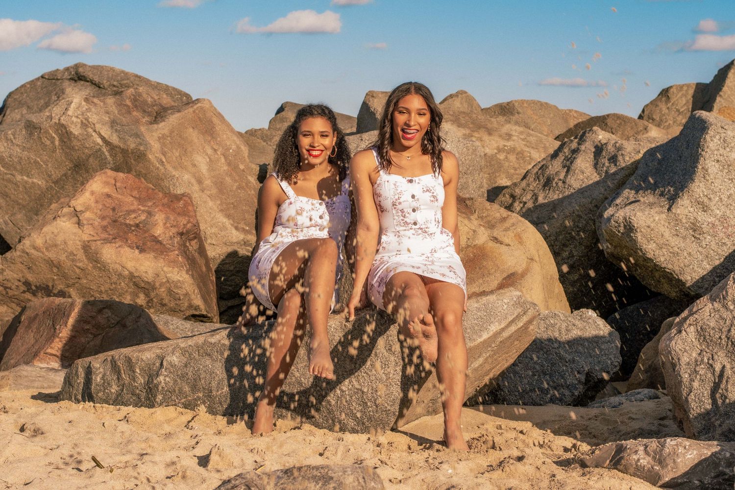 Playful beach photoshoot in Haulover, FL – siblings splashing sand while sitting on the rocks at sunset.