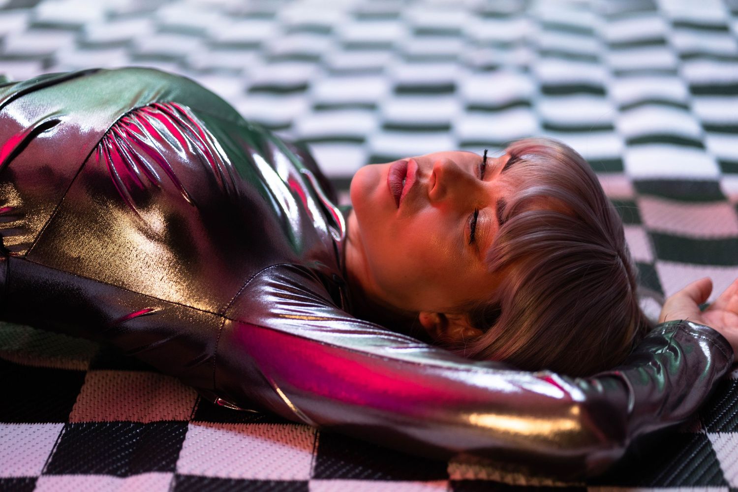 Futuristic creative fashion portrait in Fort Lauderdale, FL – woman in a metallic bodysuit lying on a checkerboard floor.