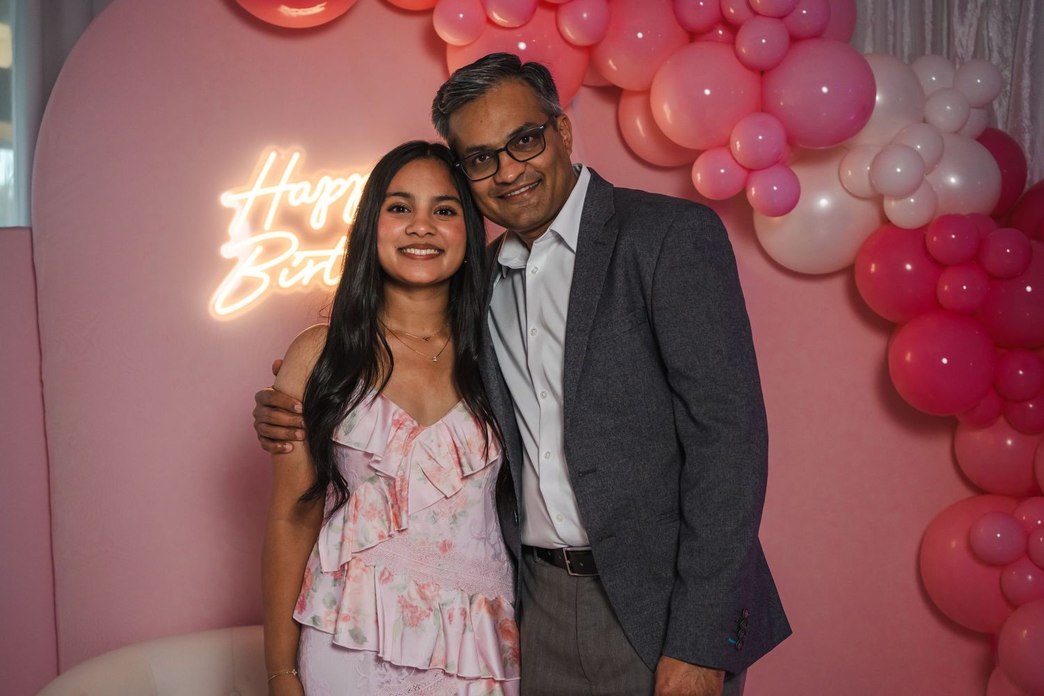 Birthday girl and guest posing in front of a pink balloon wall with neon birthday sign.